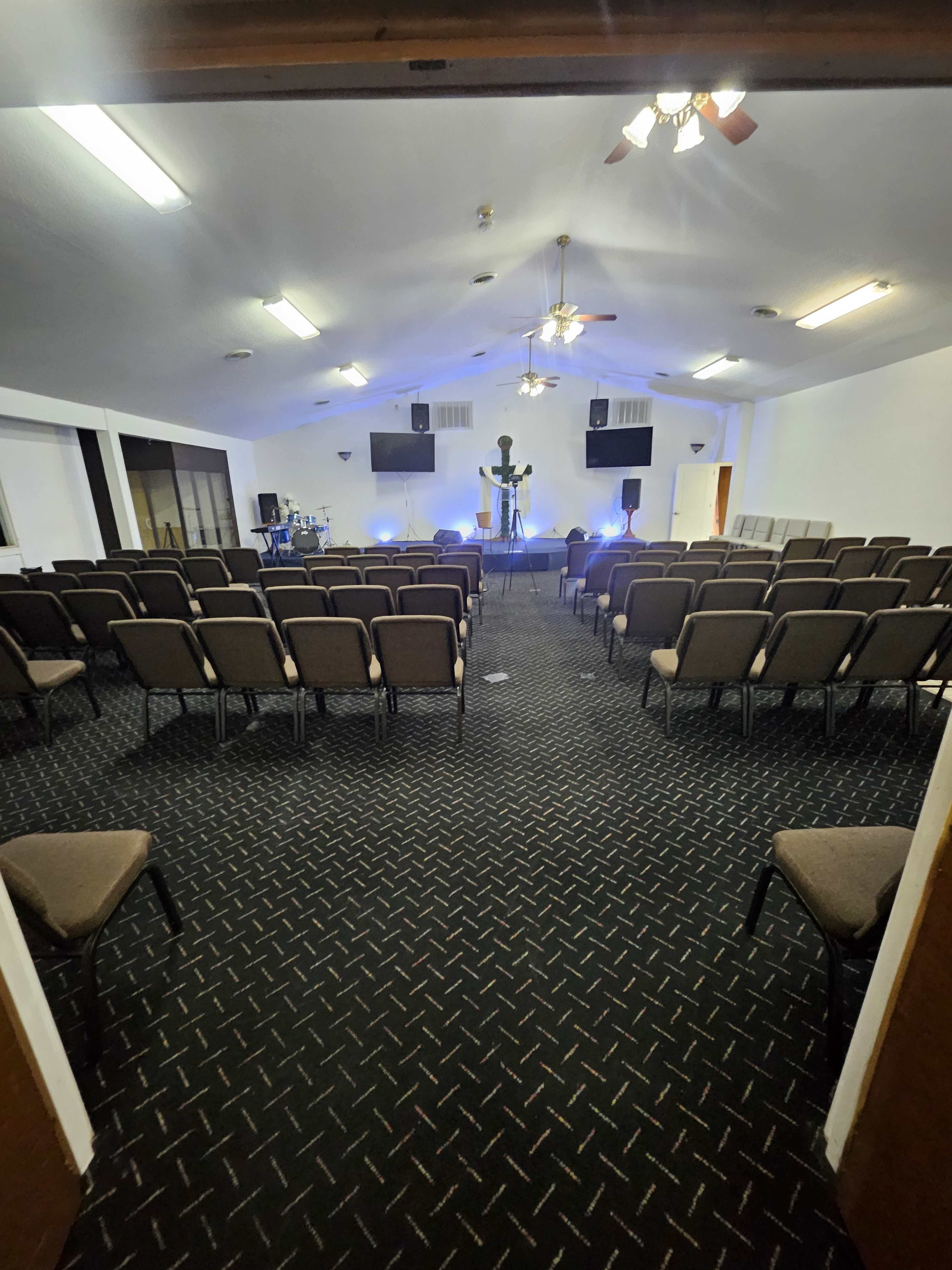The image shows the interior of a church with rows of chairs facing a stage and a cross, illuminated by blue lights.