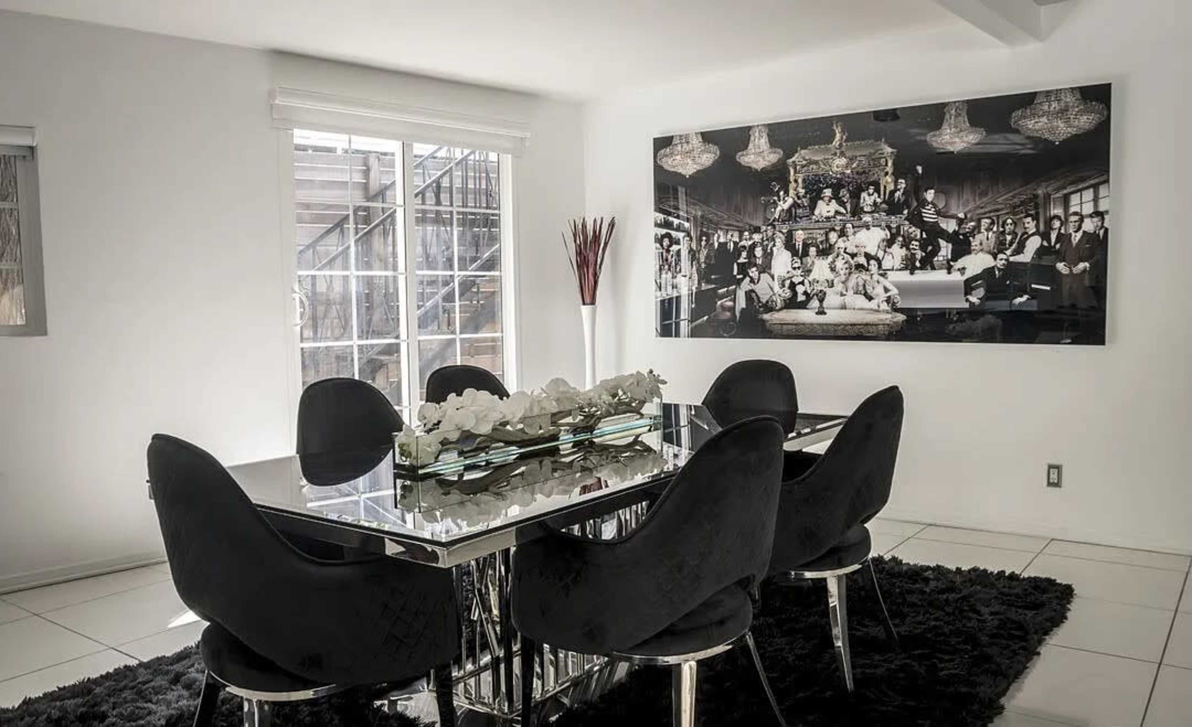 A modern dining room features a glass-top table surrounded by black chairs and is adorned with a large black-and-white photograph on the wall.
