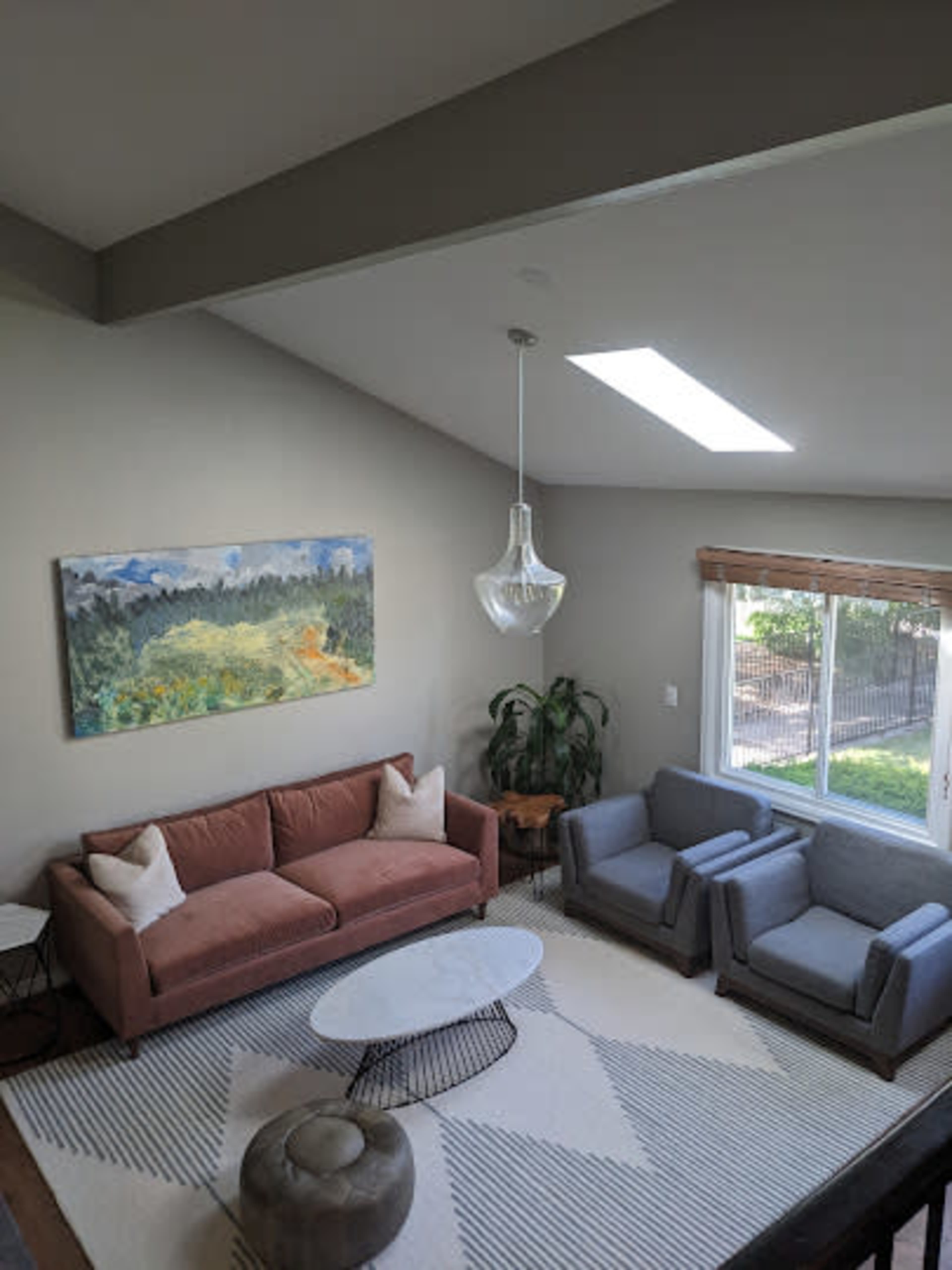 A modern living room with a pink sofa, two gray armchairs, a round coffee table, and a large window letting in natural light.