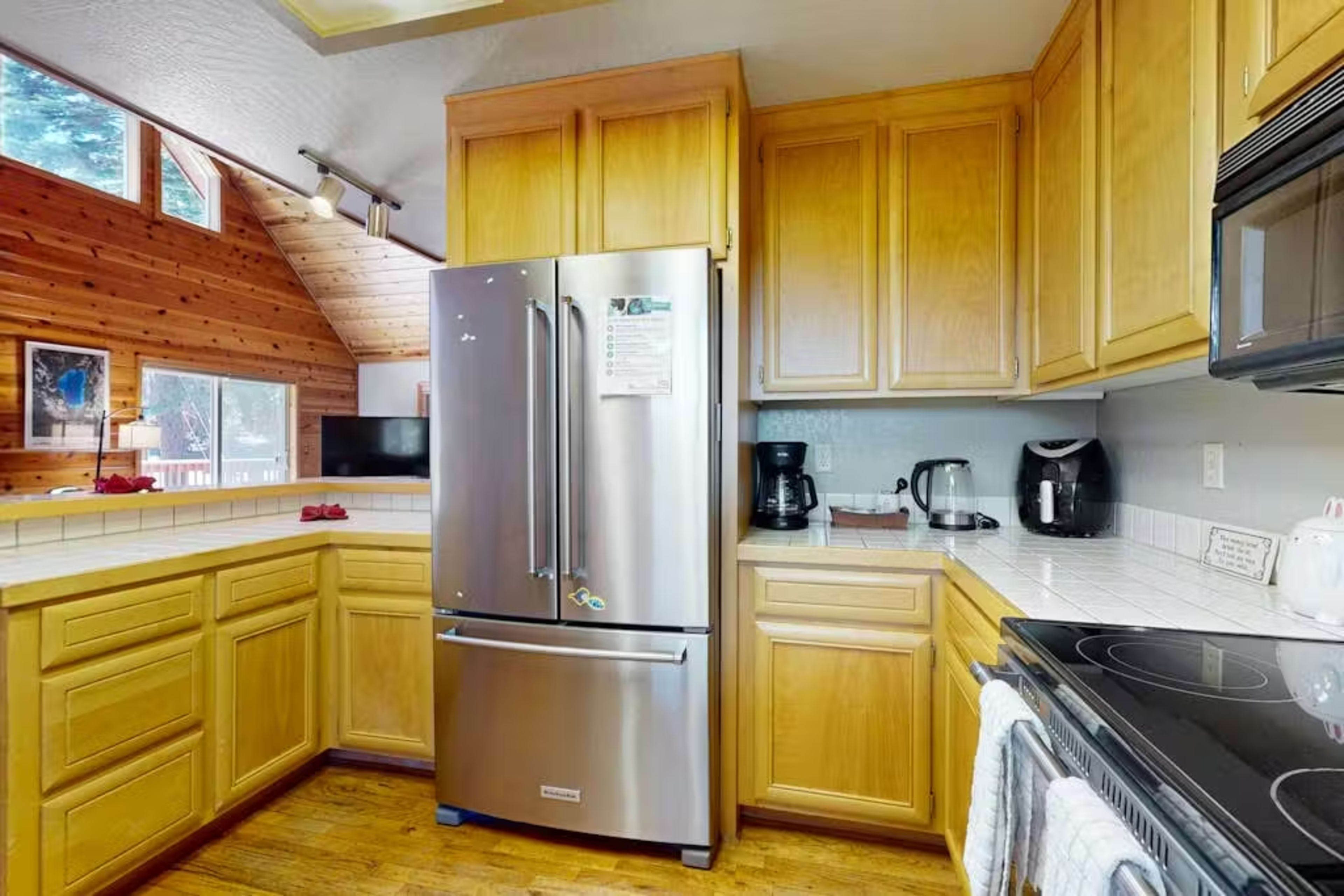 The image shows a kitchen featuring wooden cabinetry, a stainless steel refrigerator, and a countertop with an electric stove.