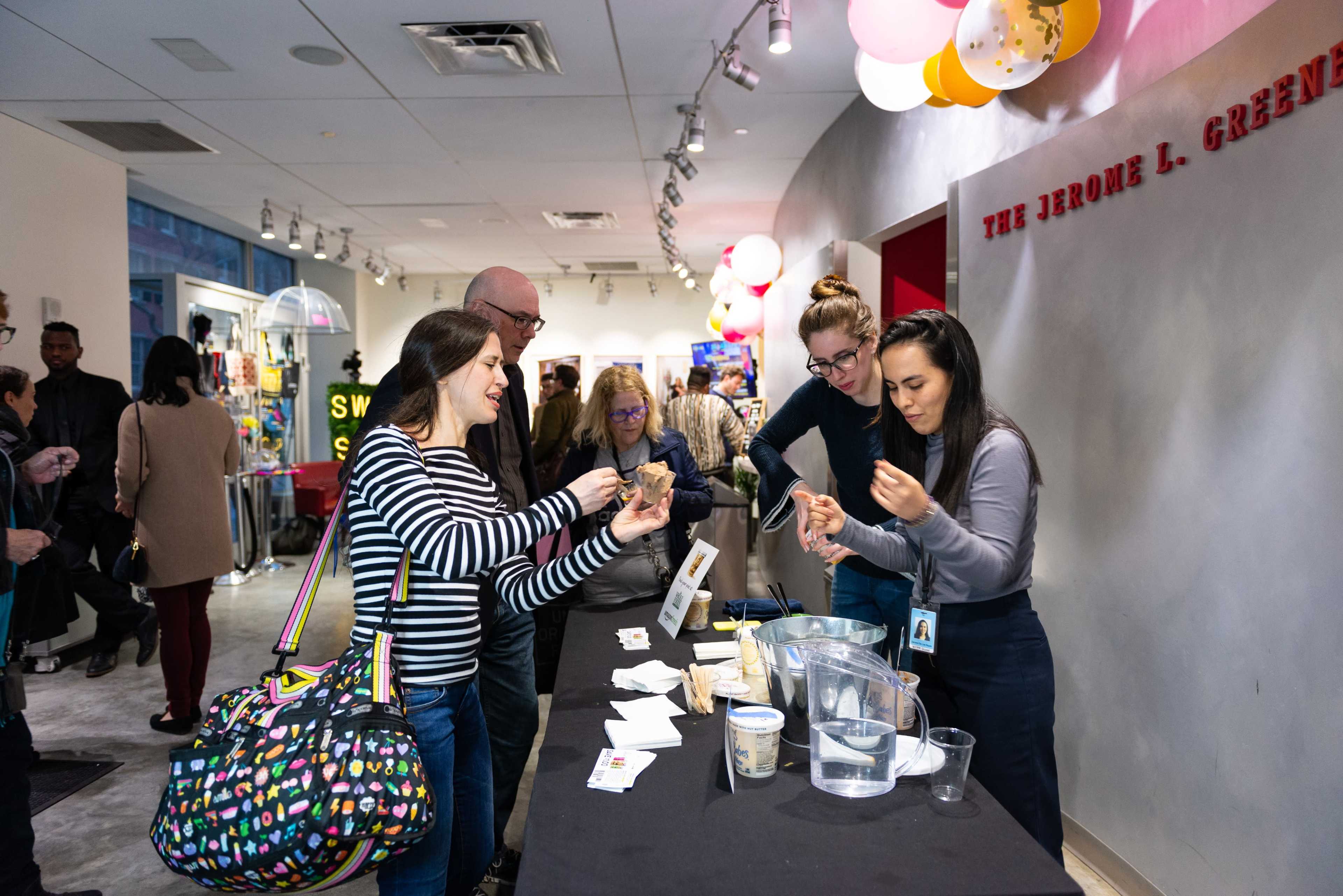 A group of people interact at a registration table during an event, handling materials and discussing.
