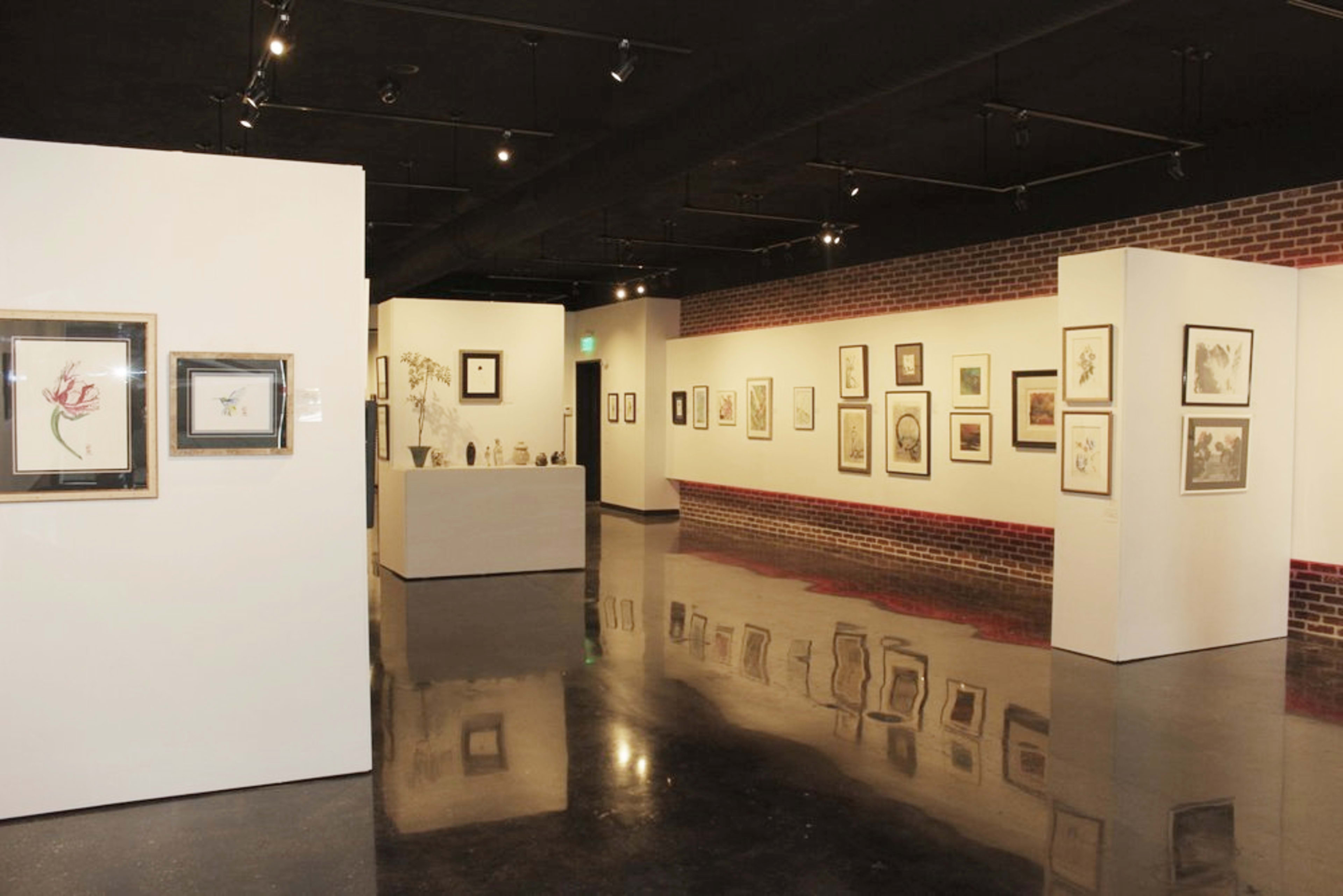 An art gallery featuring framed artwork displayed on white walls with a dark polished floor.