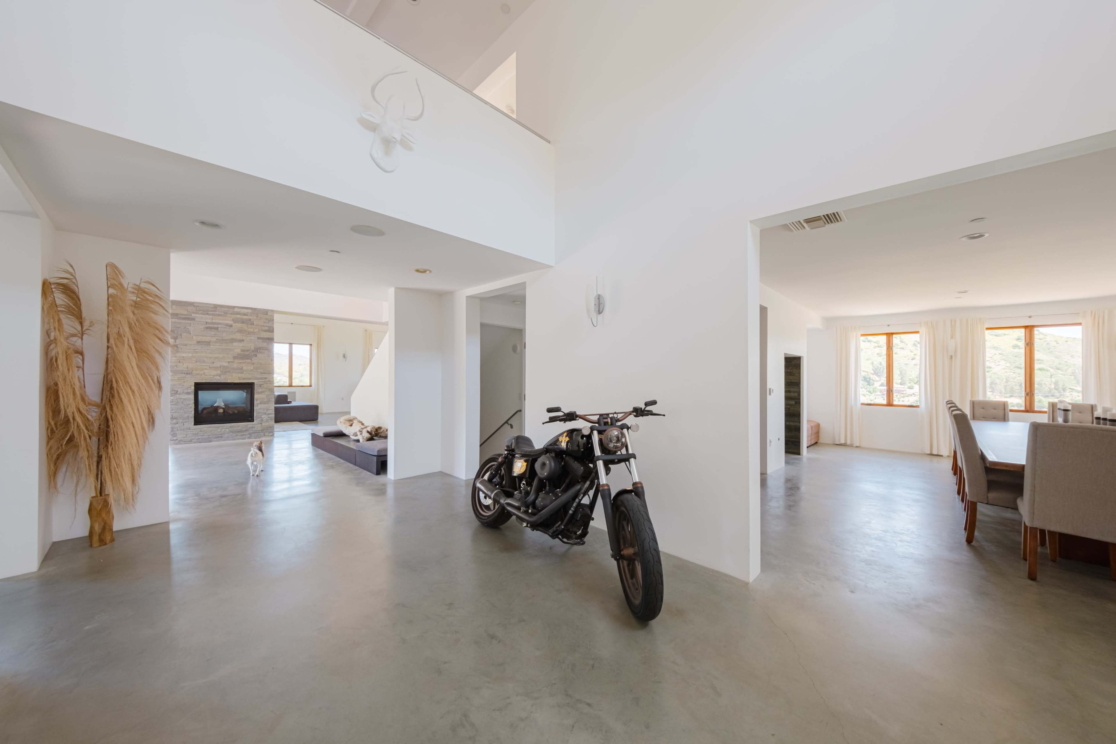 A modern, open-concept living space with a motorcycle parked on a concrete floor, featuring large windows and minimalist decor.