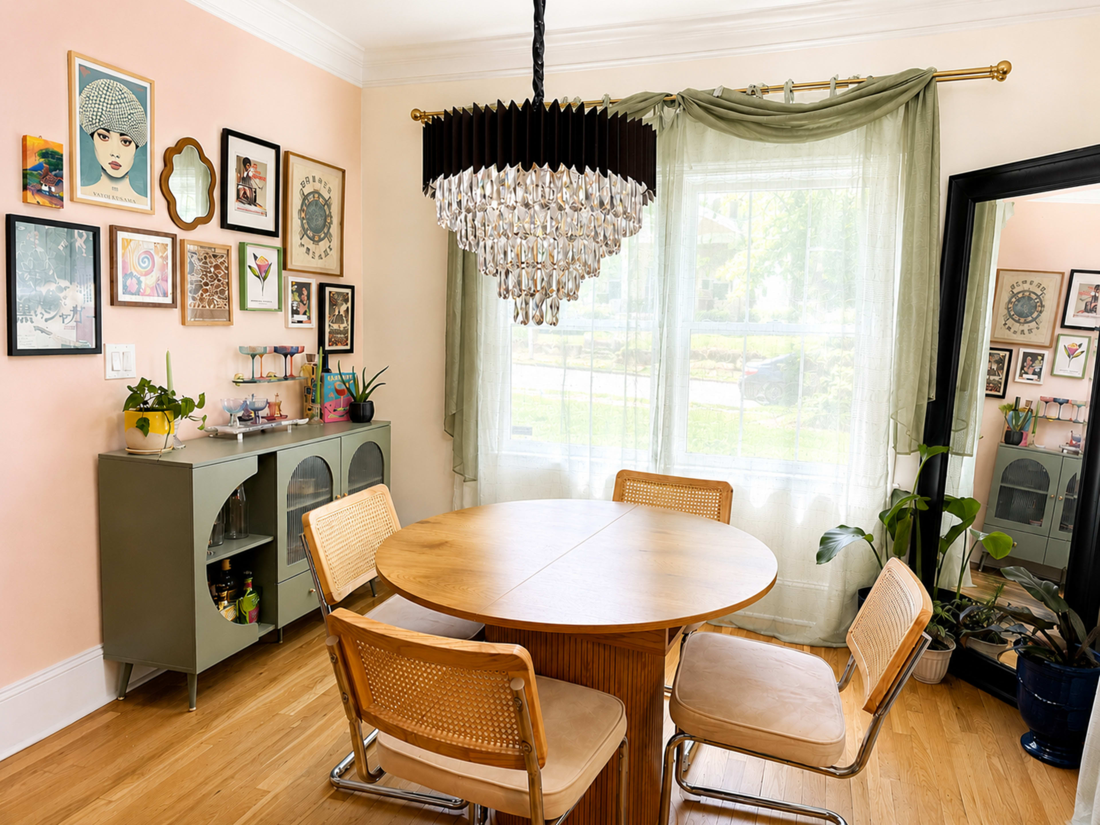 The image shows a dining area with a round wooden table, four chairs, a chandelier overhead, and walls adorned with various framed artworks.