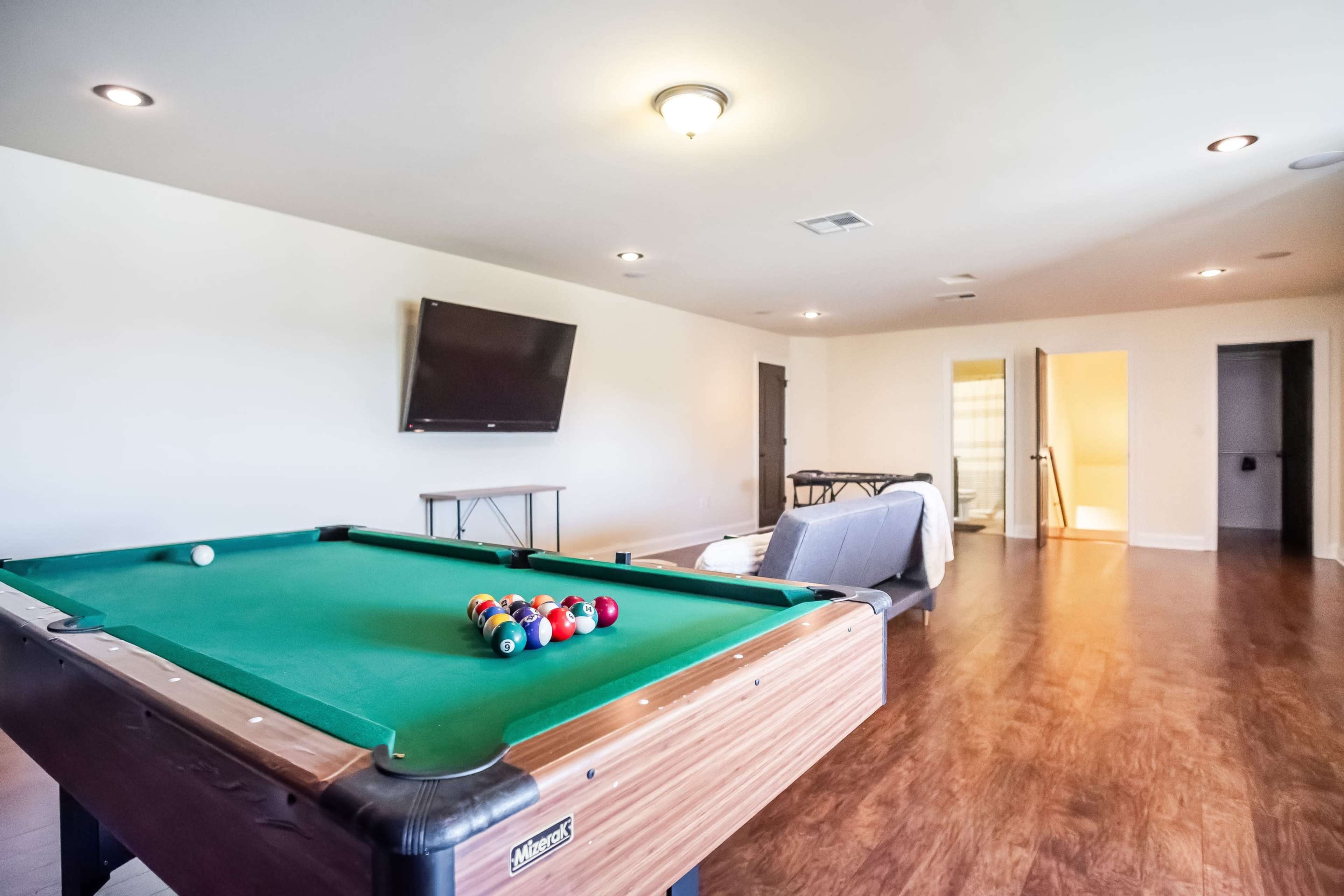 A room with a green pool table, a television mounted on the wall, and various furniture including a sofa and table.