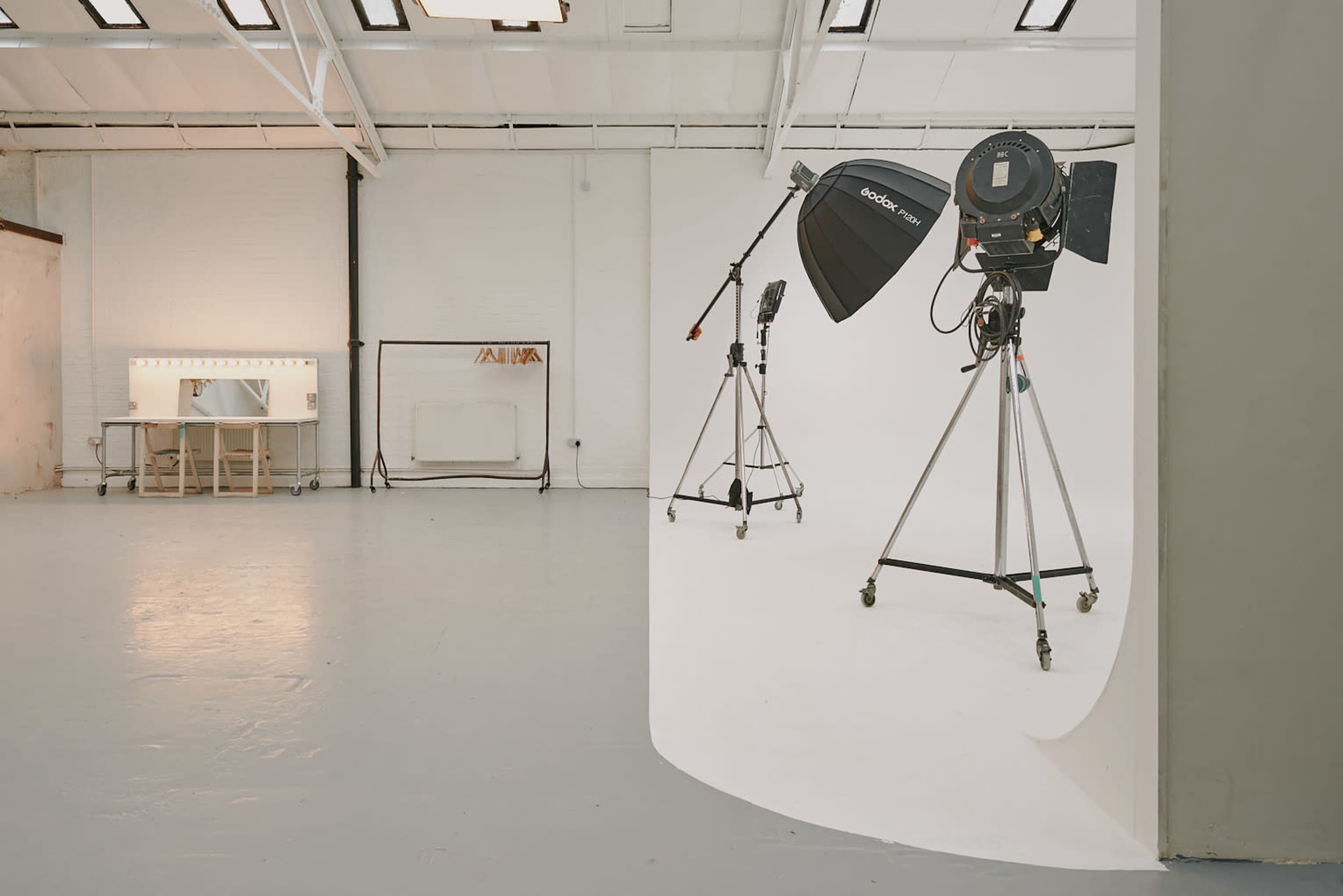 A photography studio with two light stands and a makeup station against a white backdrop.