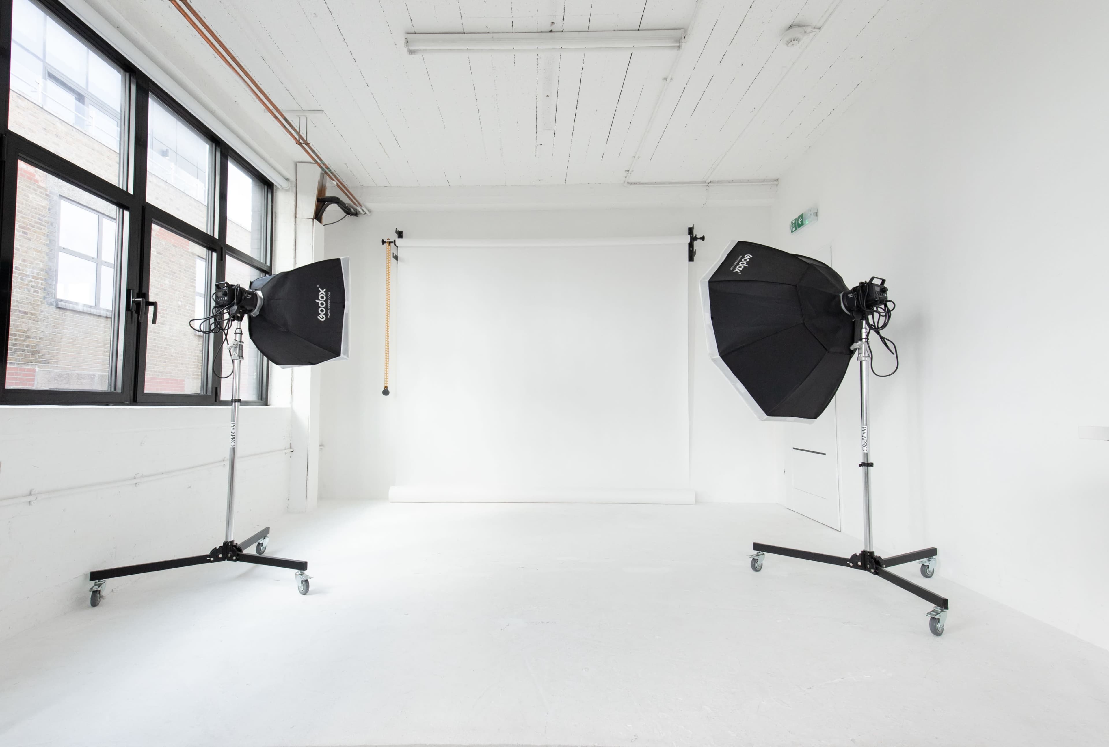 A photography studio with two light umbrellas on stands facing a blank white backdrop.