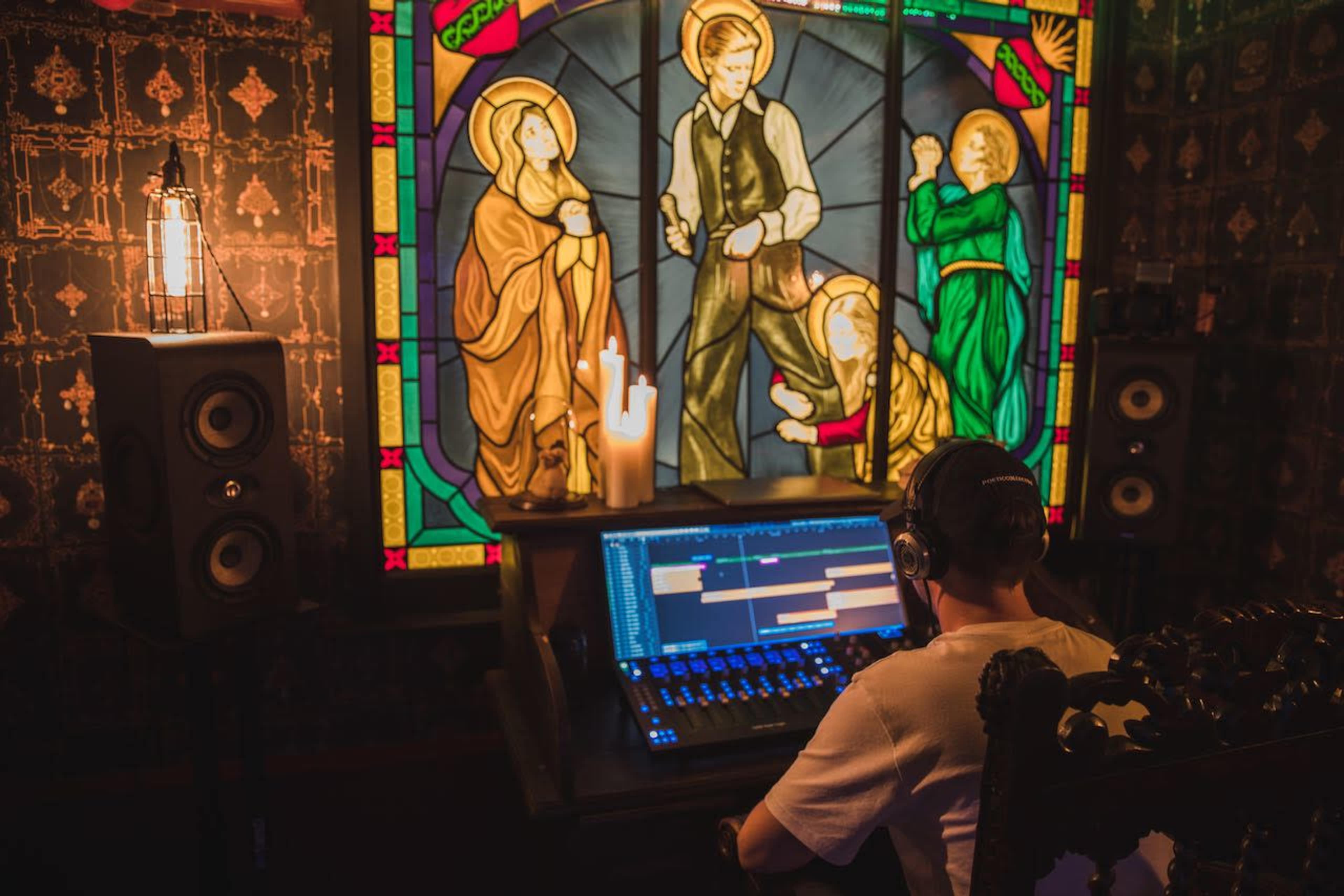 A person is sitting at a computer in a dimly lit room with stained glass windows depicting figures.