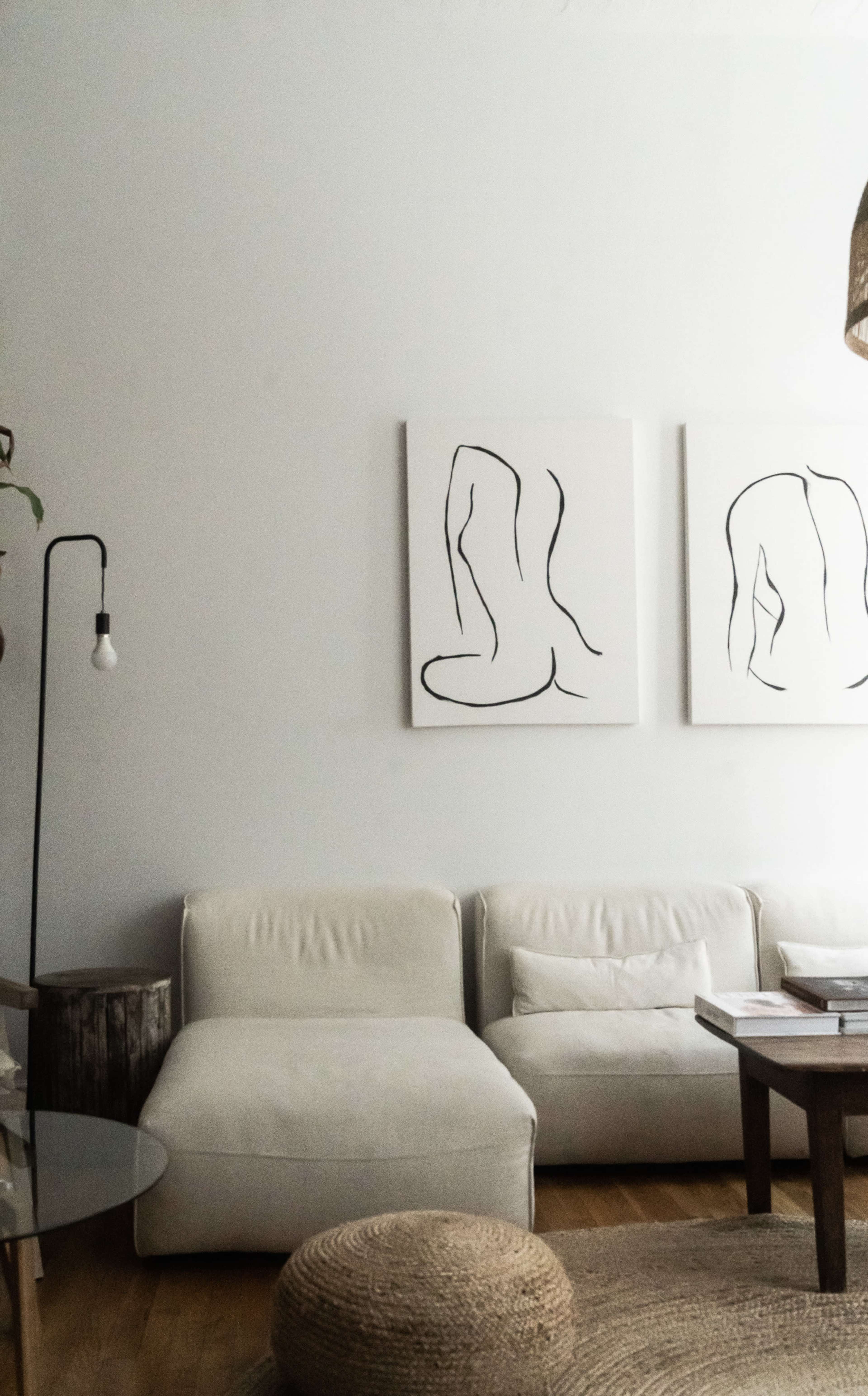 A minimalist living room with a white sectional sofa, two abstract line art paintings on the wall, a wooden coffee table, and a round woven rug.