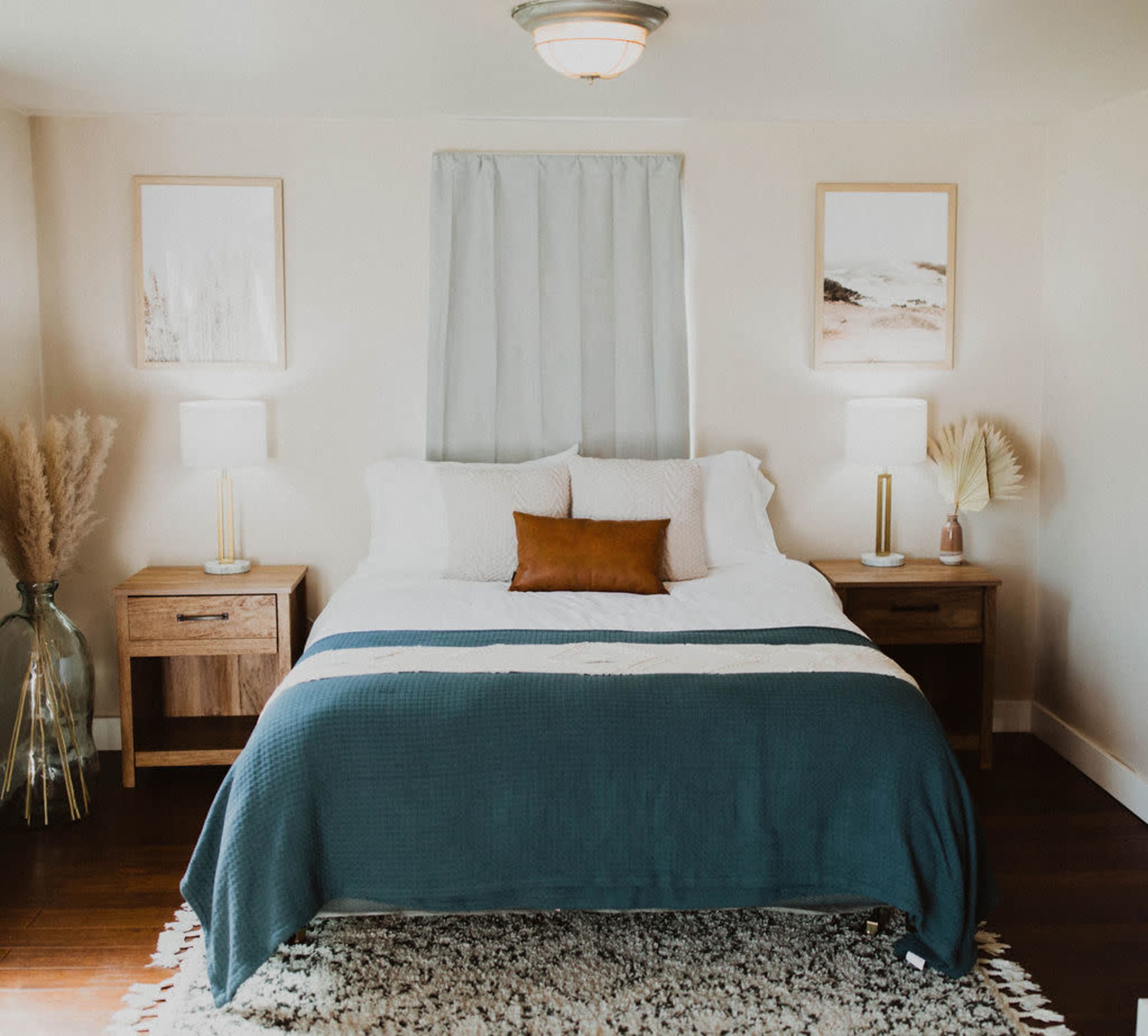 A neatly arranged bedroom featuring a bed with a dark green blanket, two bedside tables with lamps, and framed artwork on the walls.