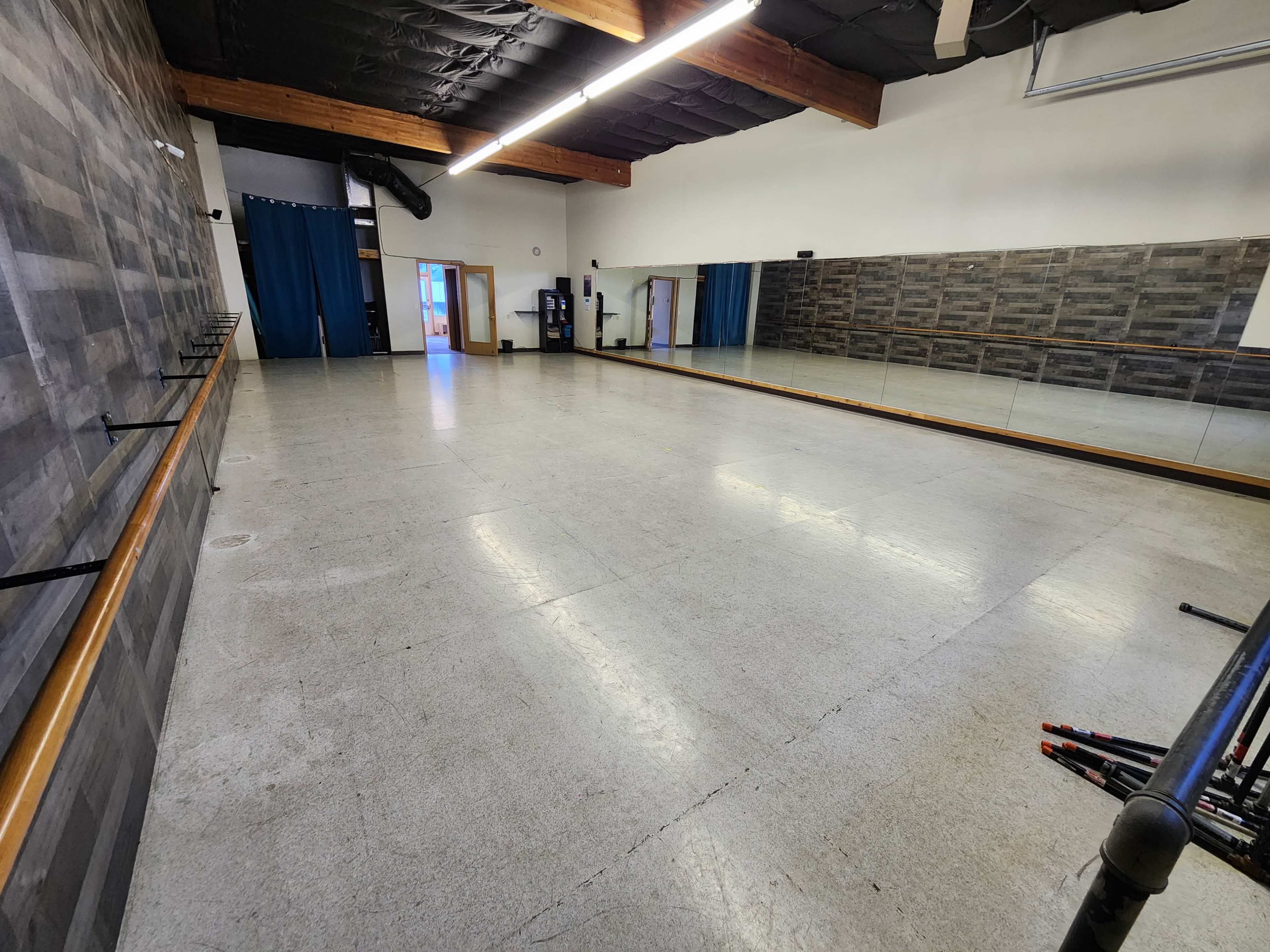 The image shows a spacious dance studio with a mirrored wall, wooden barre, and a polished floor.