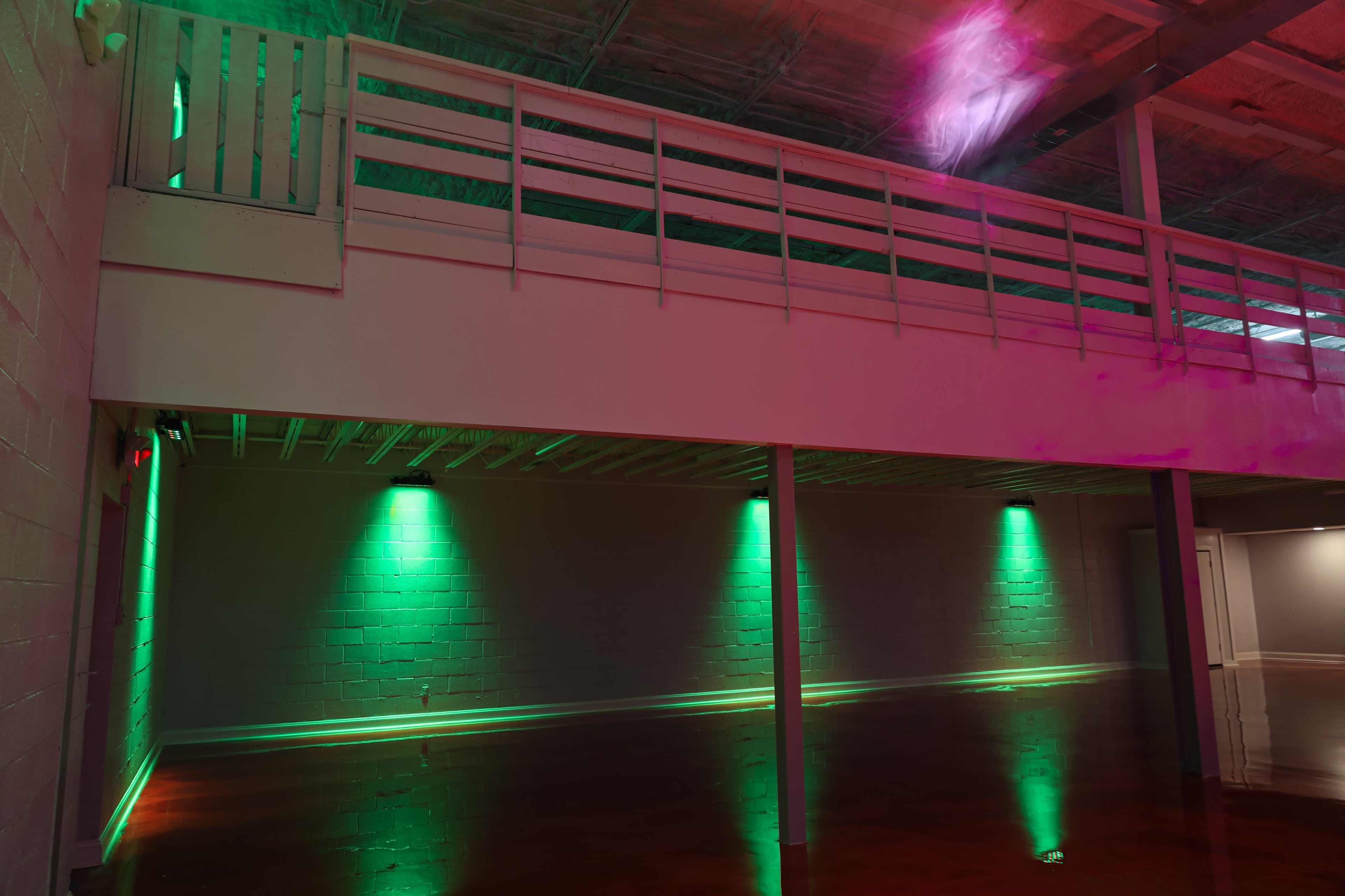 The image shows a spacious interior with a raised platform at the back, illuminated by green lights reflecting off a polished floor.