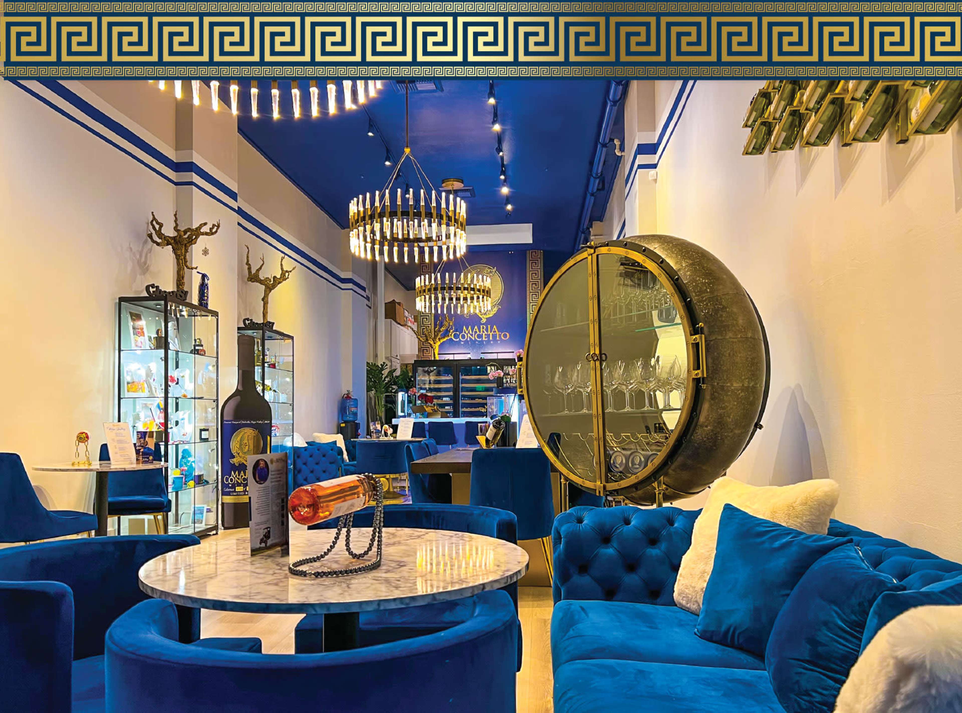The interior of a stylish lounge features blue velvet furniture, a marble table, and elegant light fixtures.