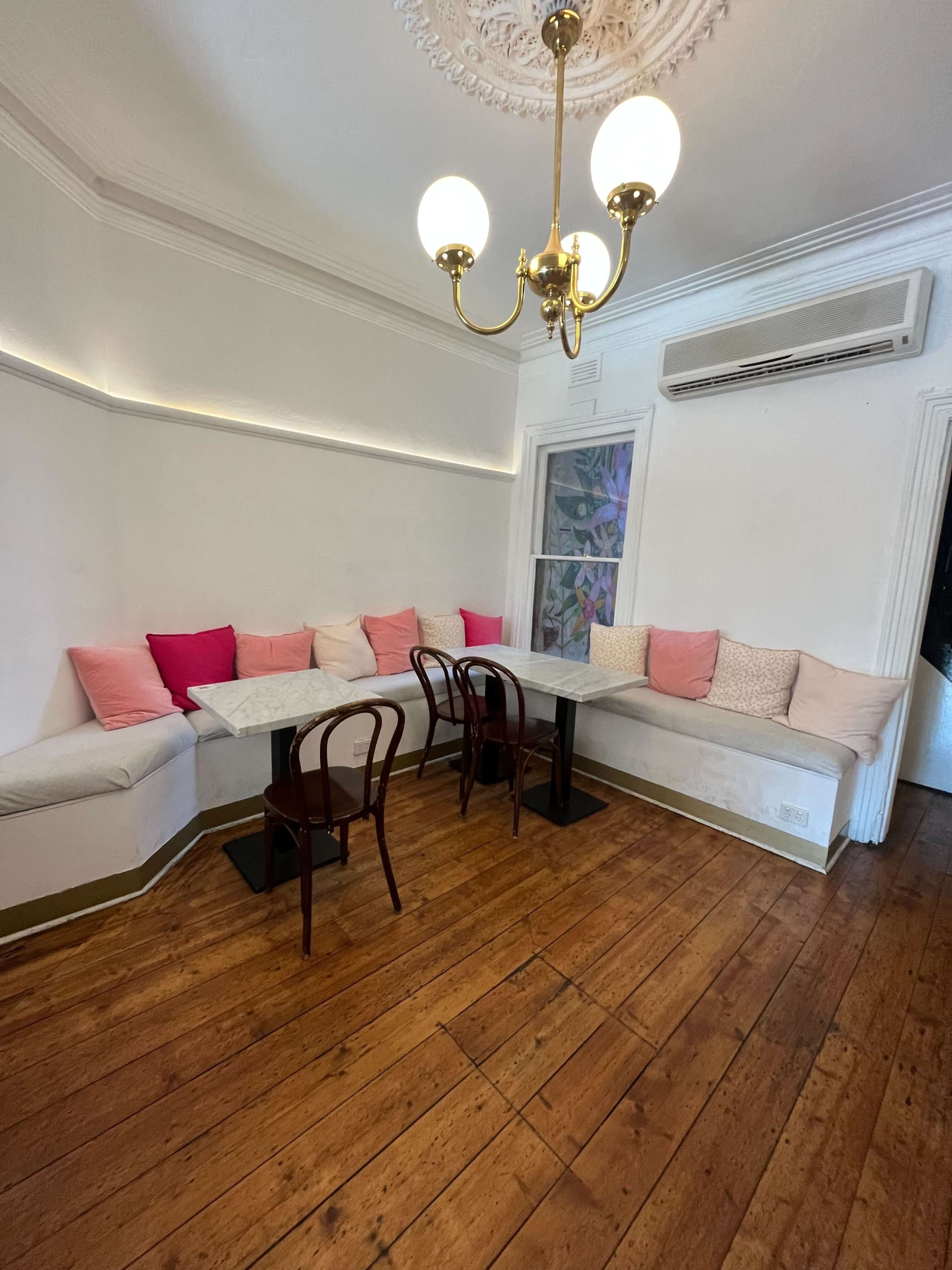 The image shows a cozy cafe interior with a curved bench seating area along the wall, a couple of black tables, and wooden flooring.