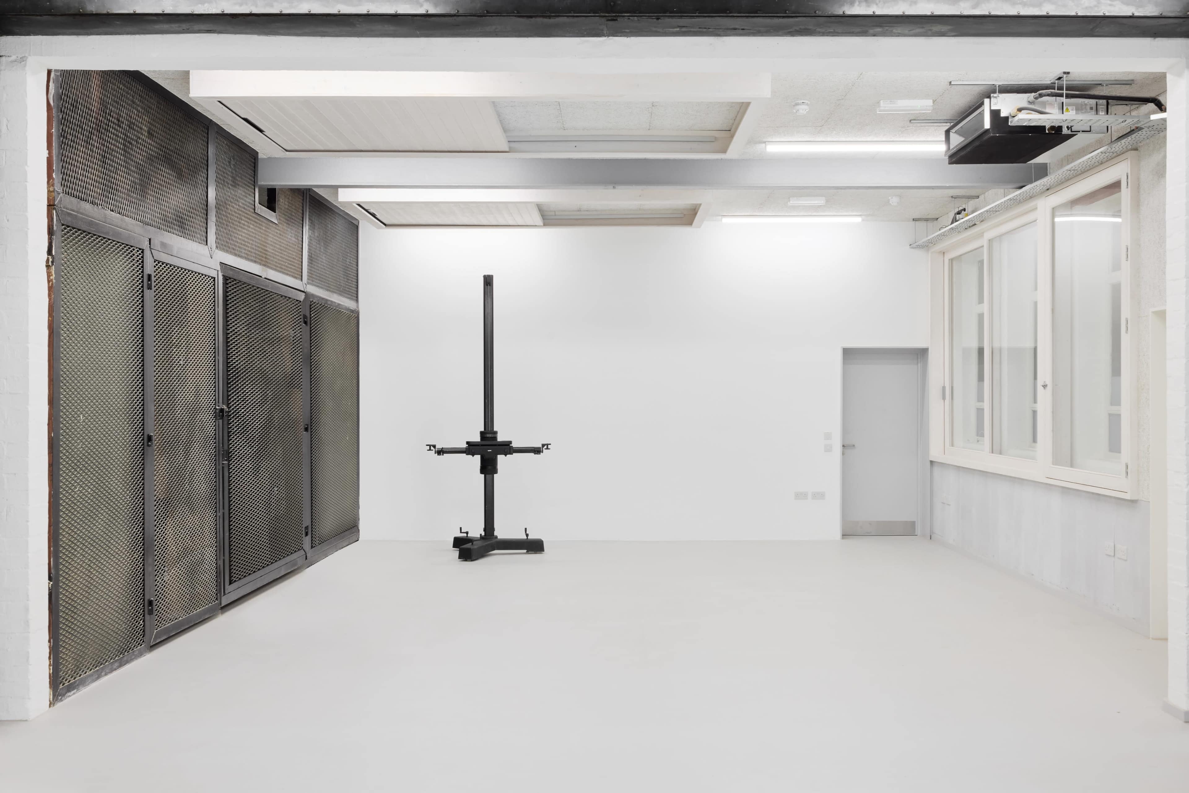 The image shows a spacious, minimally furnished room with a tall, black vertical structure and industrial-style metal panels on one side.