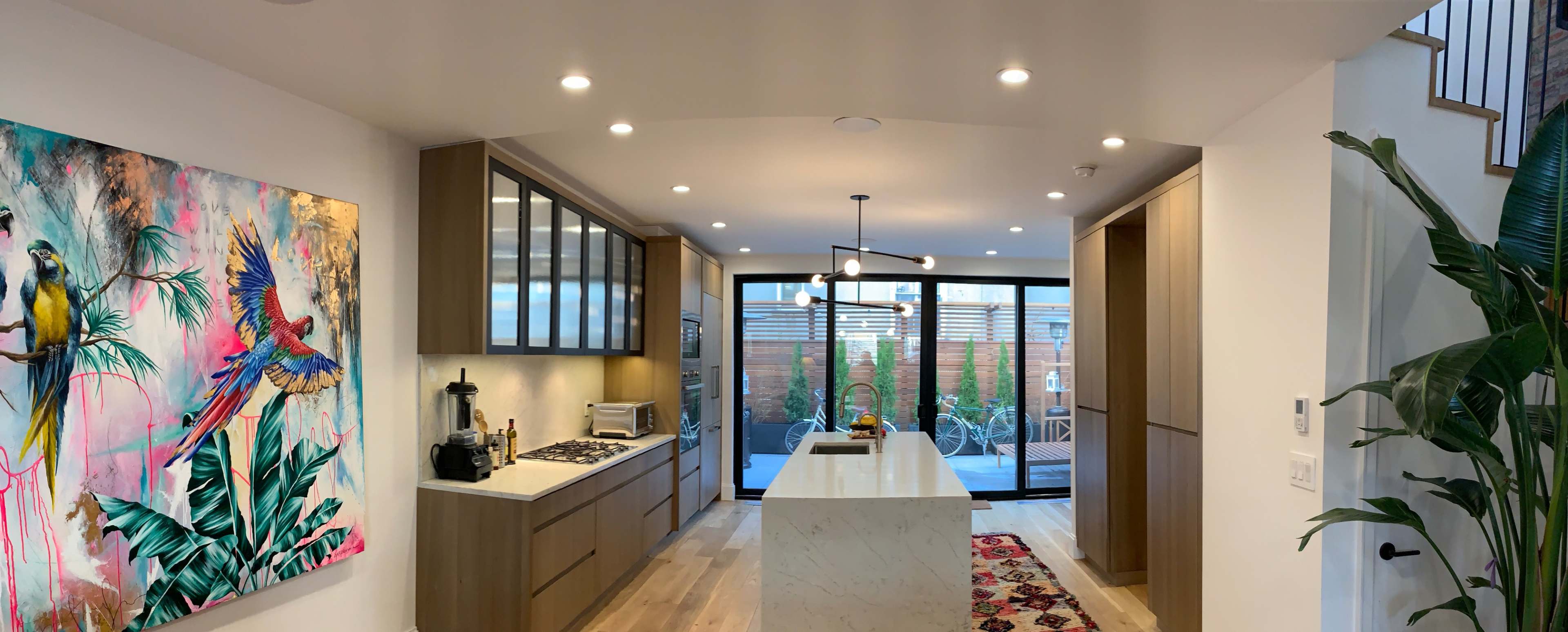 A modern kitchen with wooden cabinetry, a central marble island, and glass doors opening to an outdoor patio.