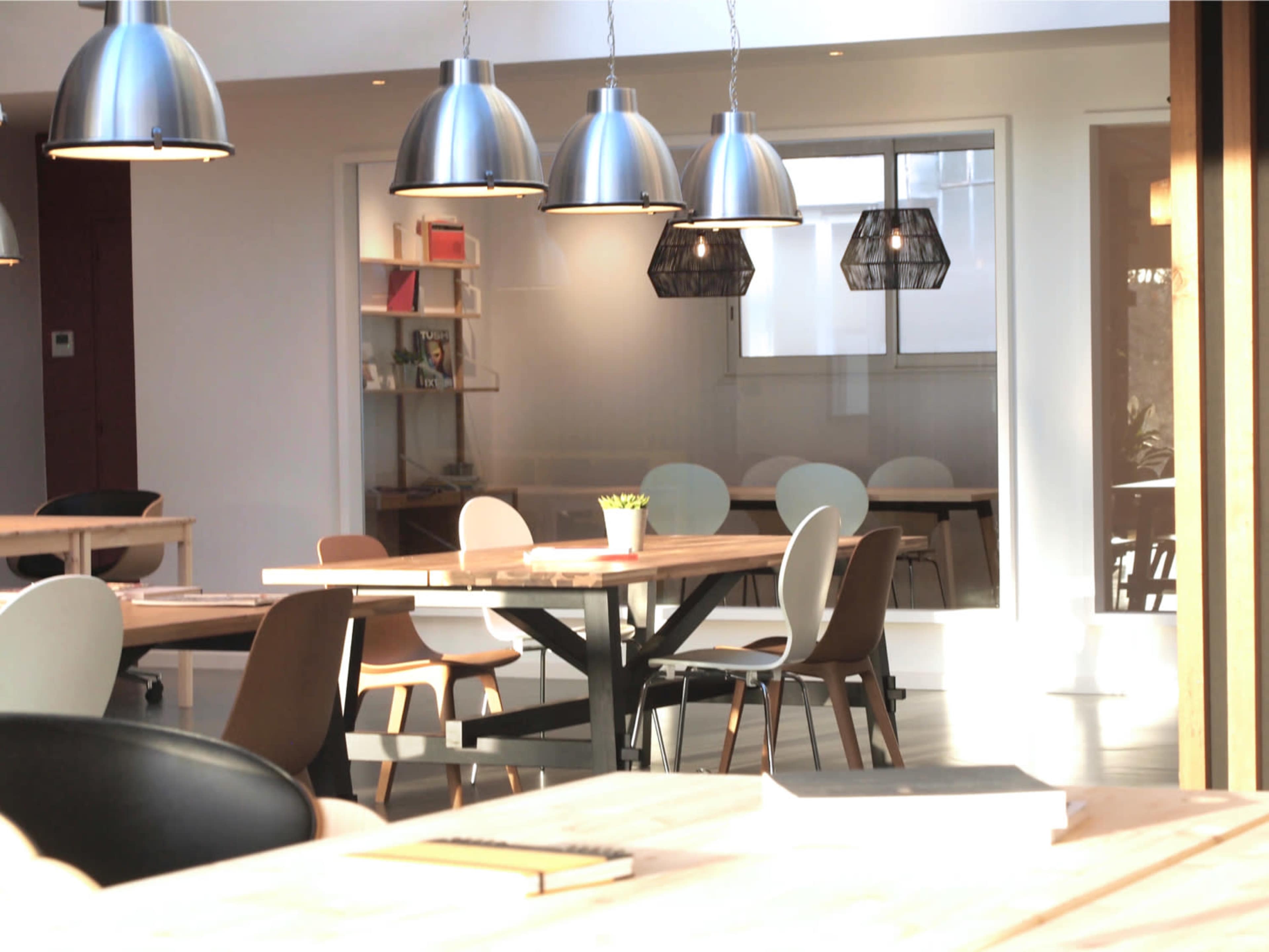 A modern office space with wooden tables, various chairs, and pendant lighting.
