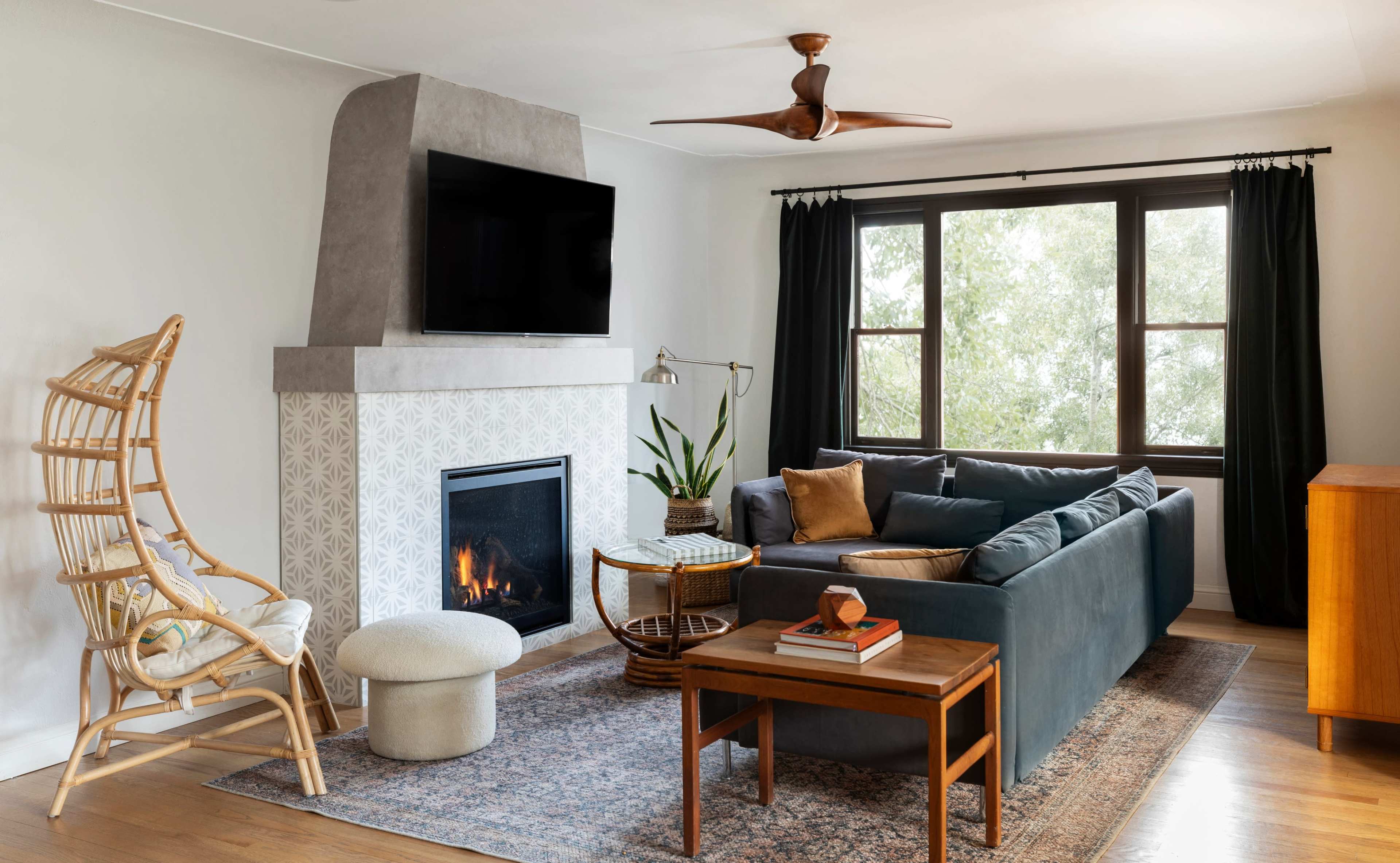 The living room features a comfortable sofa, a coffee table, a fireplace with a TV mounted above, and a tall window with dark curtains.