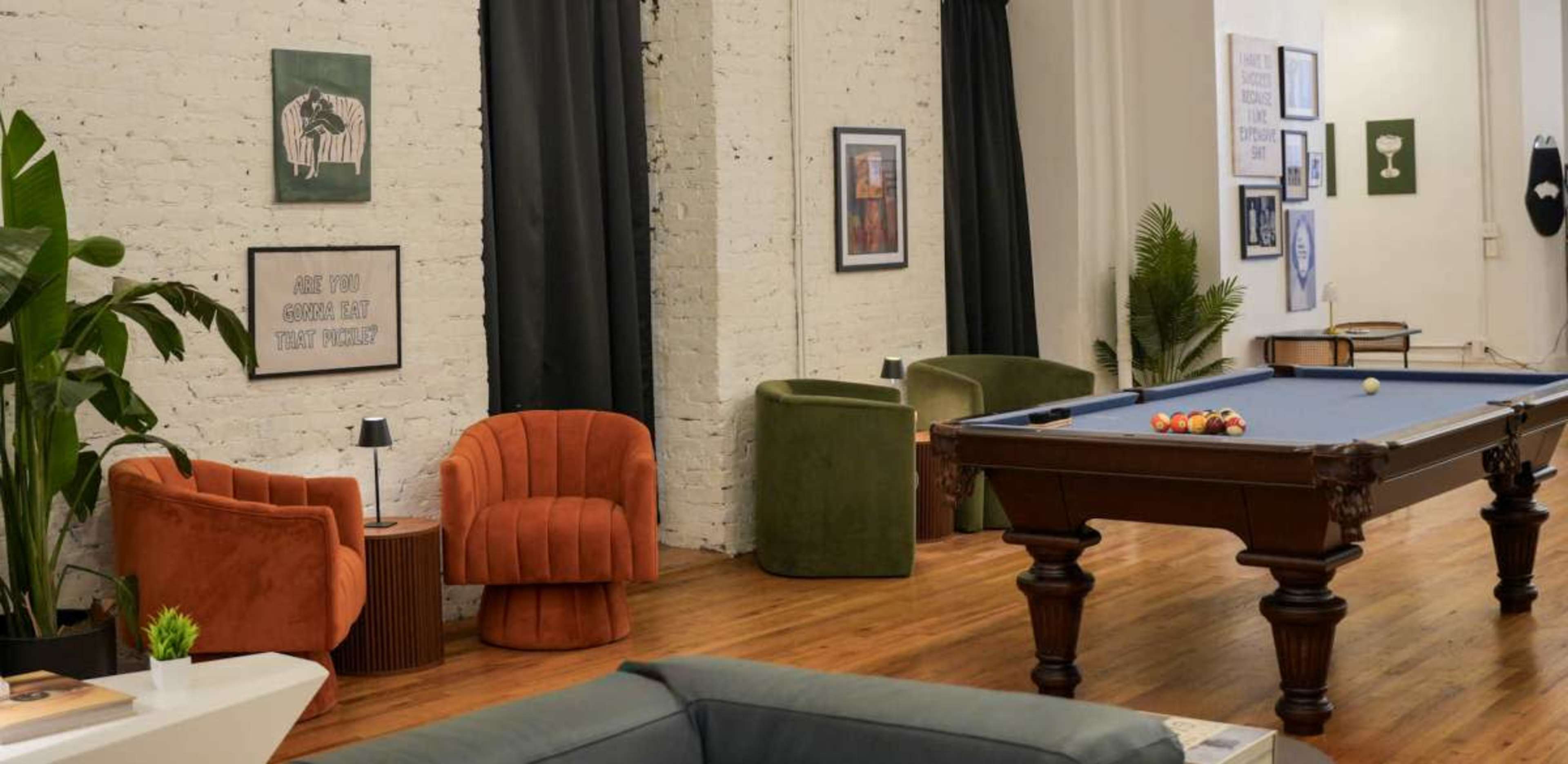 The image shows a stylish lounge area with a billiard table, surrounded by various seating options and decorative wall art.