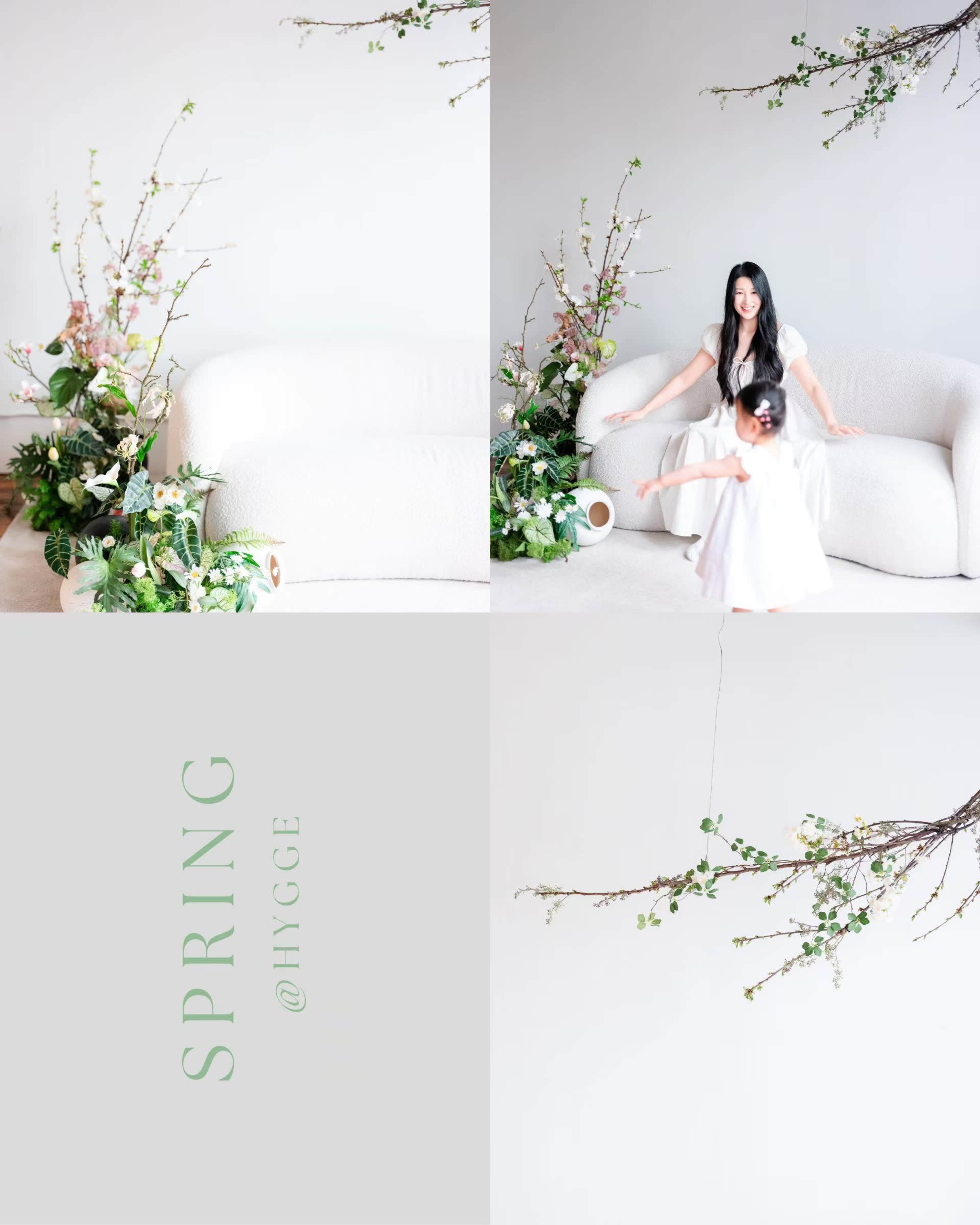A woman and a child are playing in a spacious, softly decorated living room adorned with spring flowers and branches.