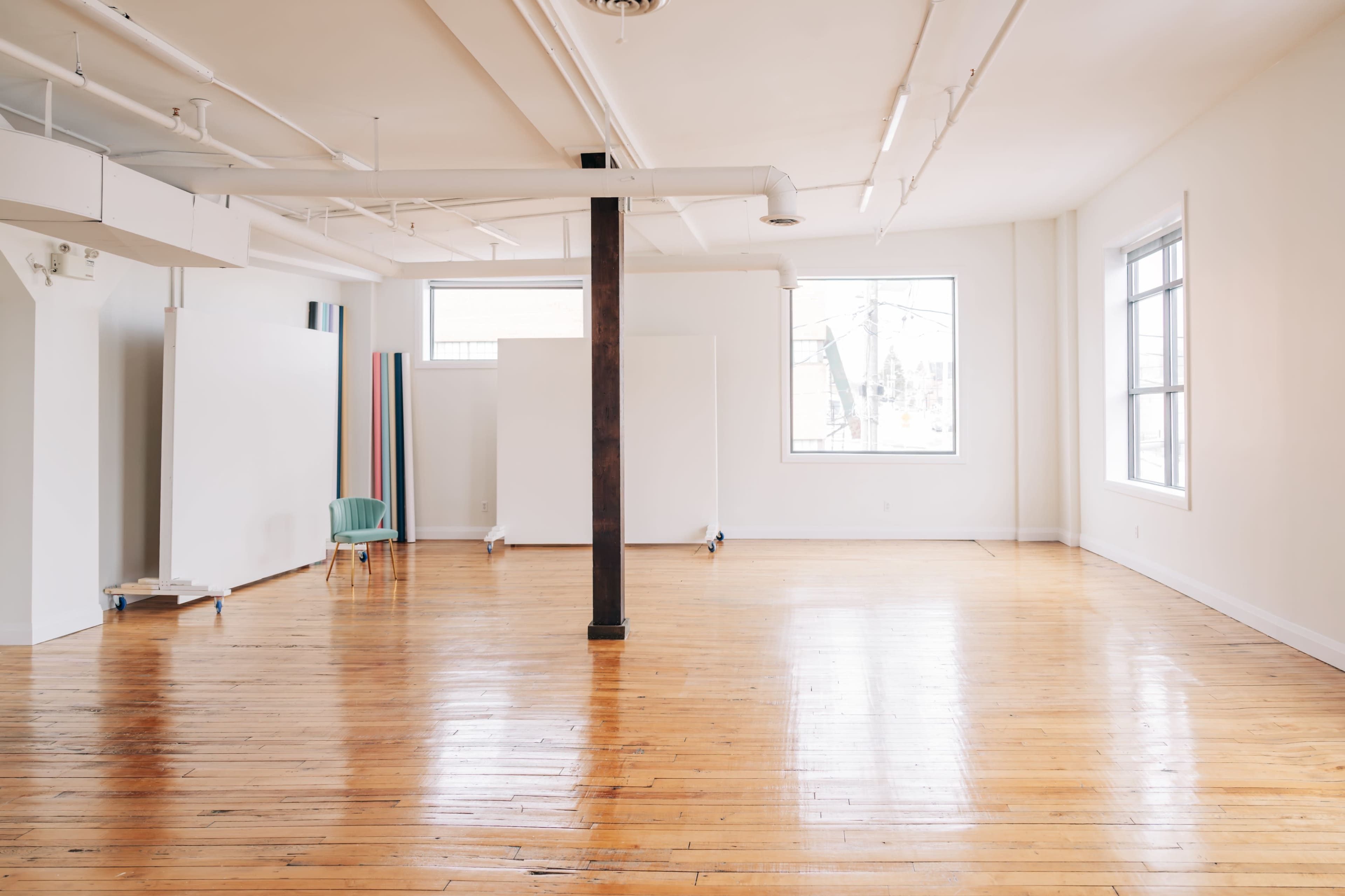 A spacious, empty room with polished wooden floors, white walls, and a single column in the center holding the ceiling.