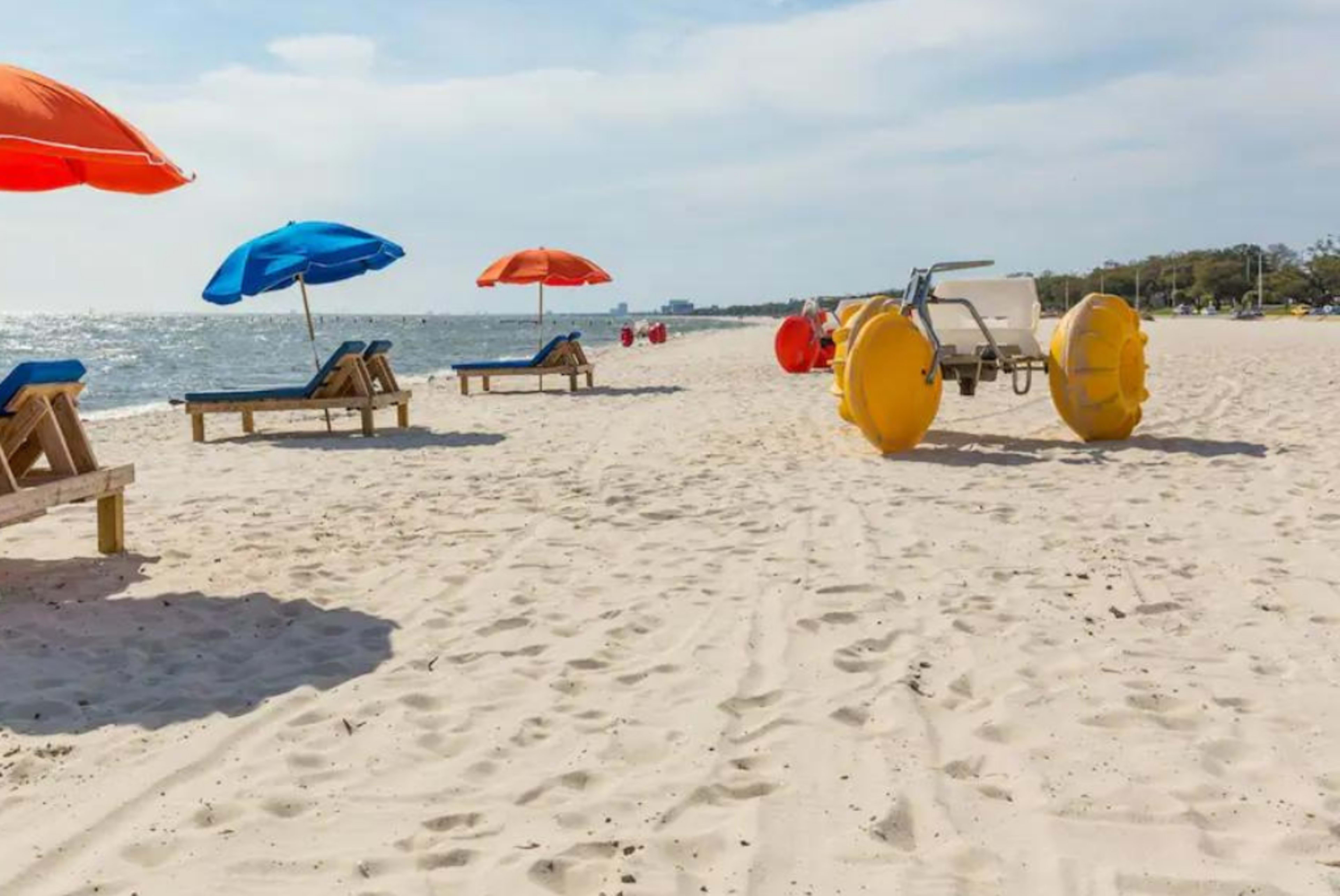 A sandy beach with wooden lounge chairs, colorful umbrellas, and a beach vehicle near the shoreline.