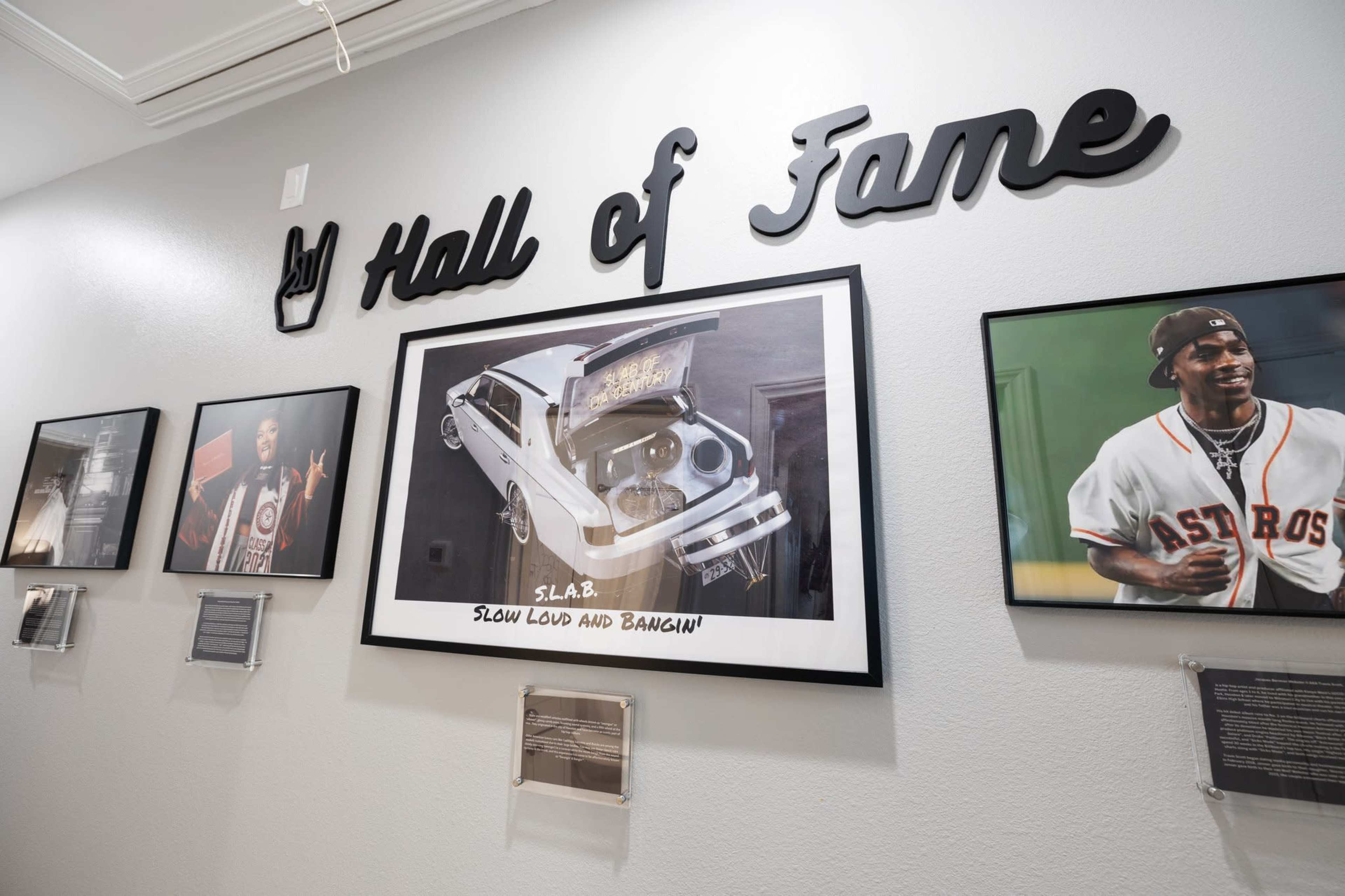 A wall labeled "Hall of Fame" featuring framed art and photographs, including a picture of a customized car and images of individuals, presumably artists or musicians.