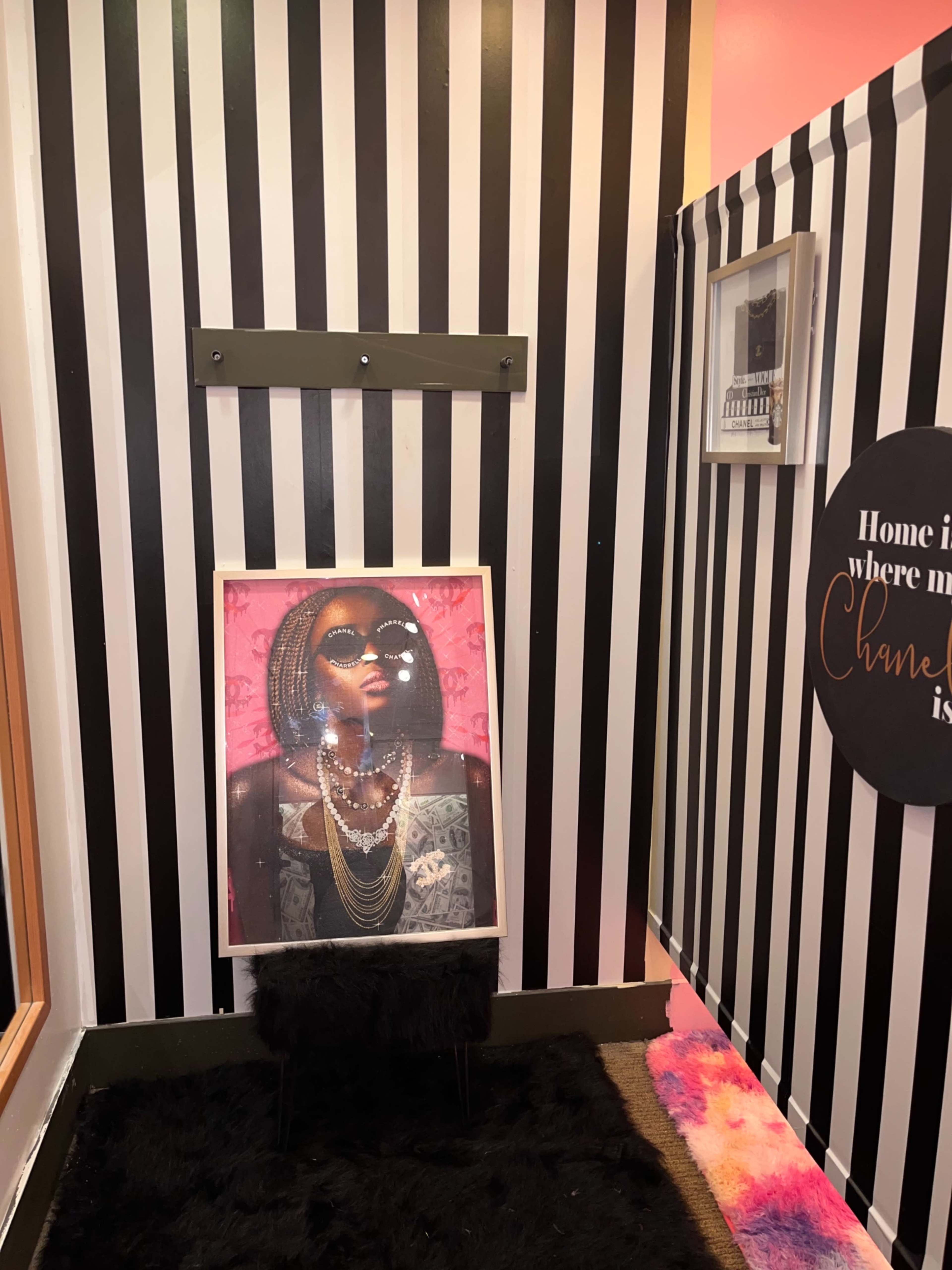 A corner of a room with black and white striped walls, featuring a framed portrait of a woman on a stand surrounded by decorative elements.
