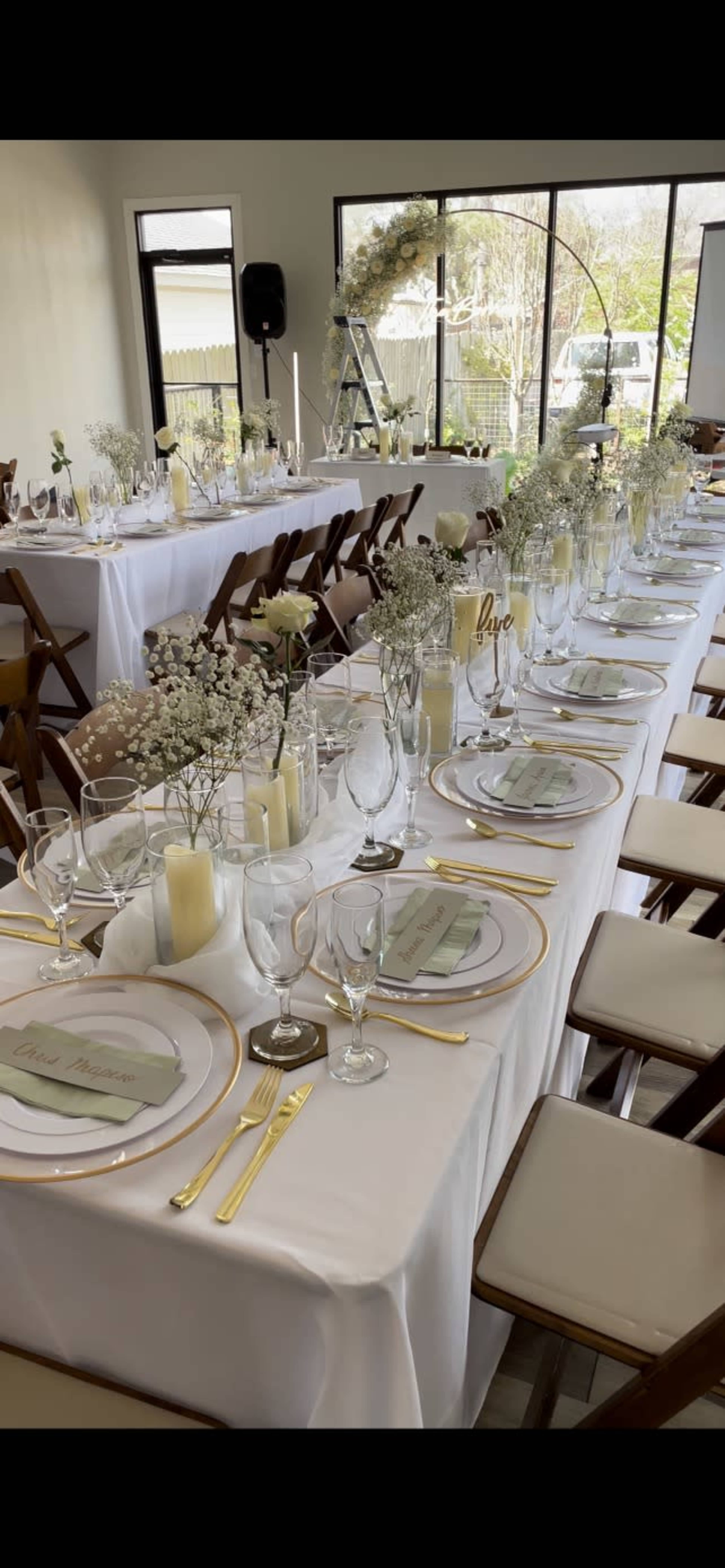 A long banquet table is set with elegant place settings, floral centerpieces, and candles, all arranged in a well-lit event space.