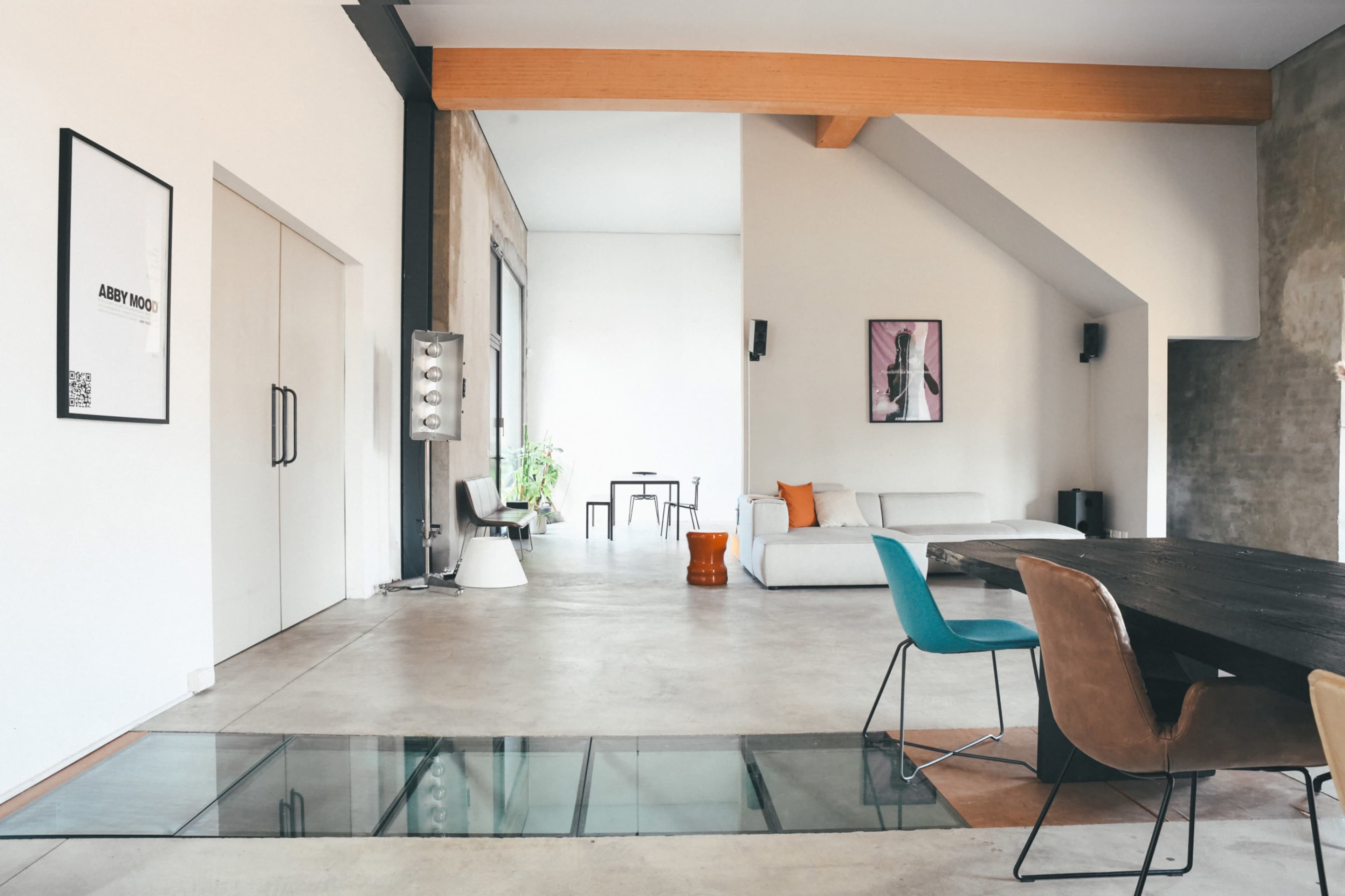 The image shows a modern interior space featuring a minimalist design with a dining table, colorful chairs, and a simple living area.