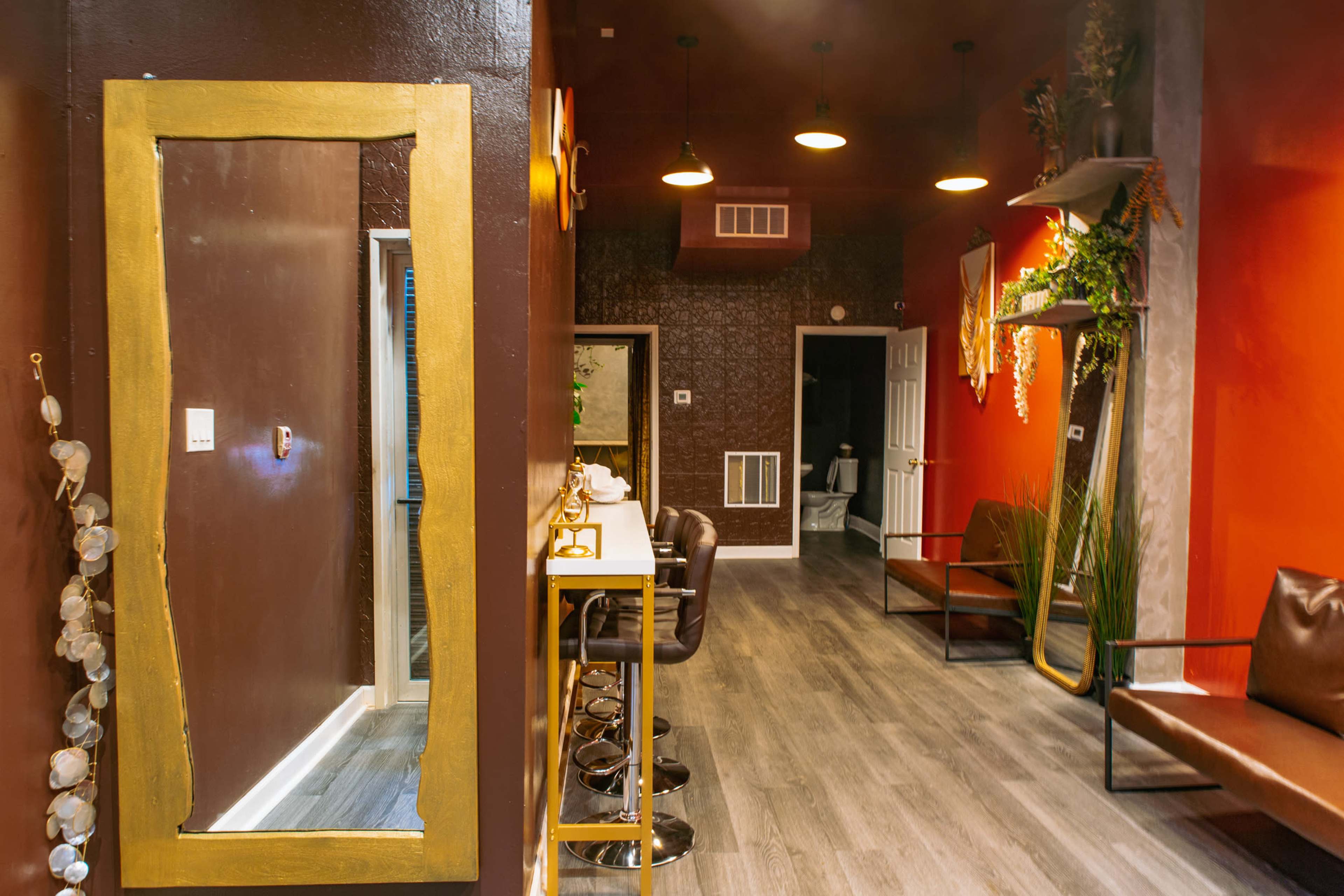 A trendy interior space featuring a hallway with a large framed mirror, a bar-height table with stools, and seating areas against the walls.