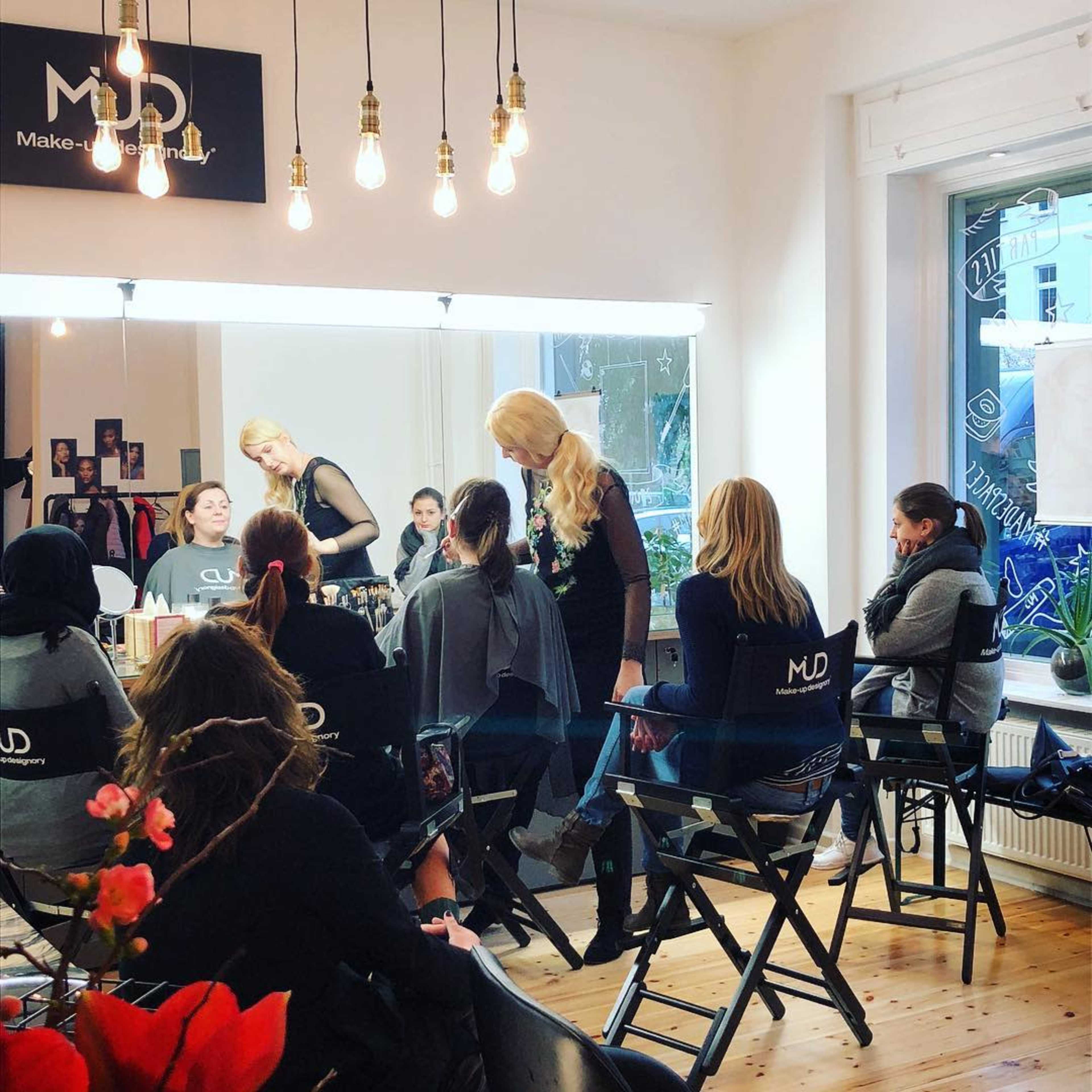 A group of women is participating in a makeup workshop in a studio with professional lighting and chairs.