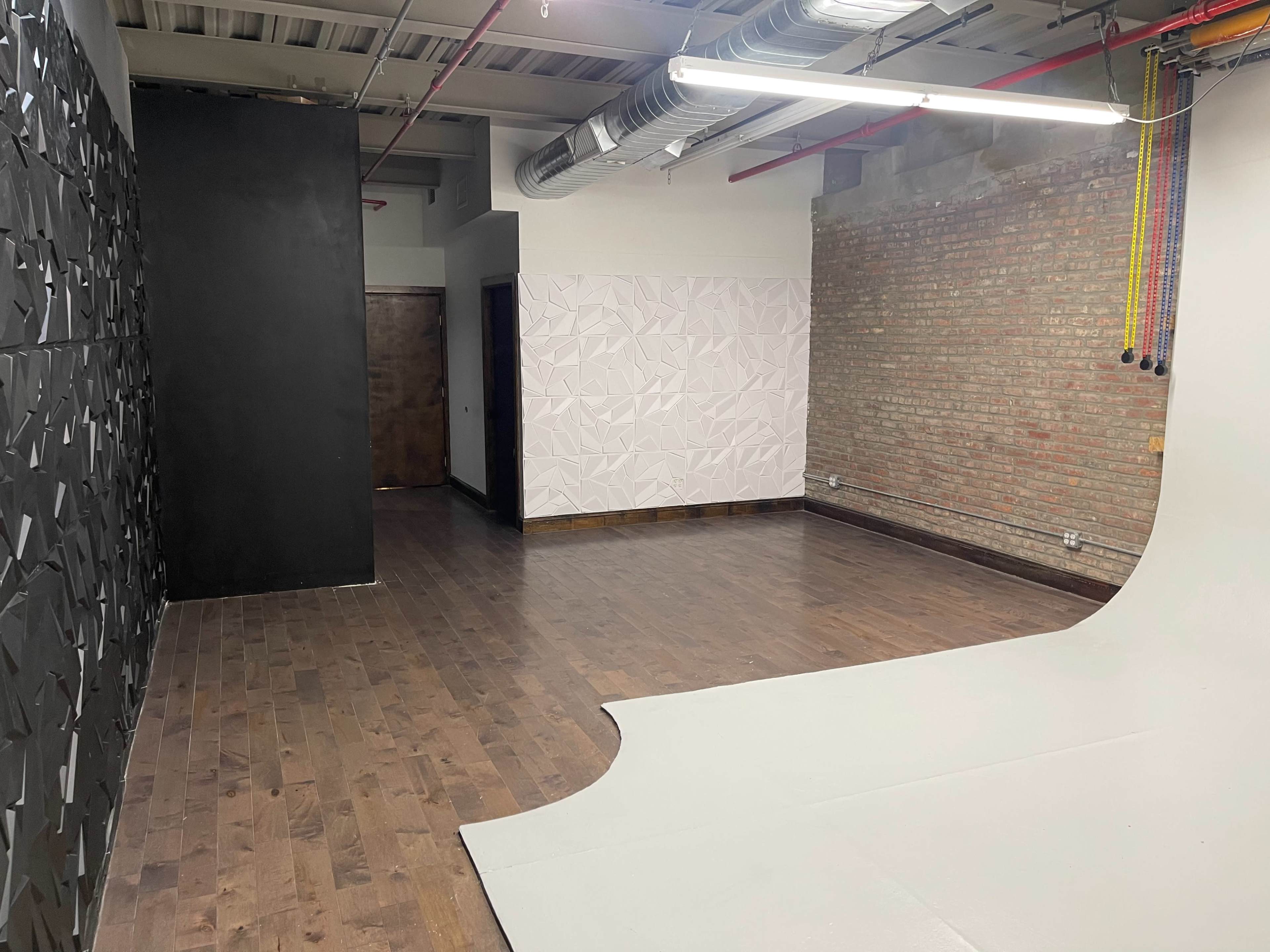 An empty studio space with wooden flooring, featuring textured black and white walls and a curved seamless backdrop.