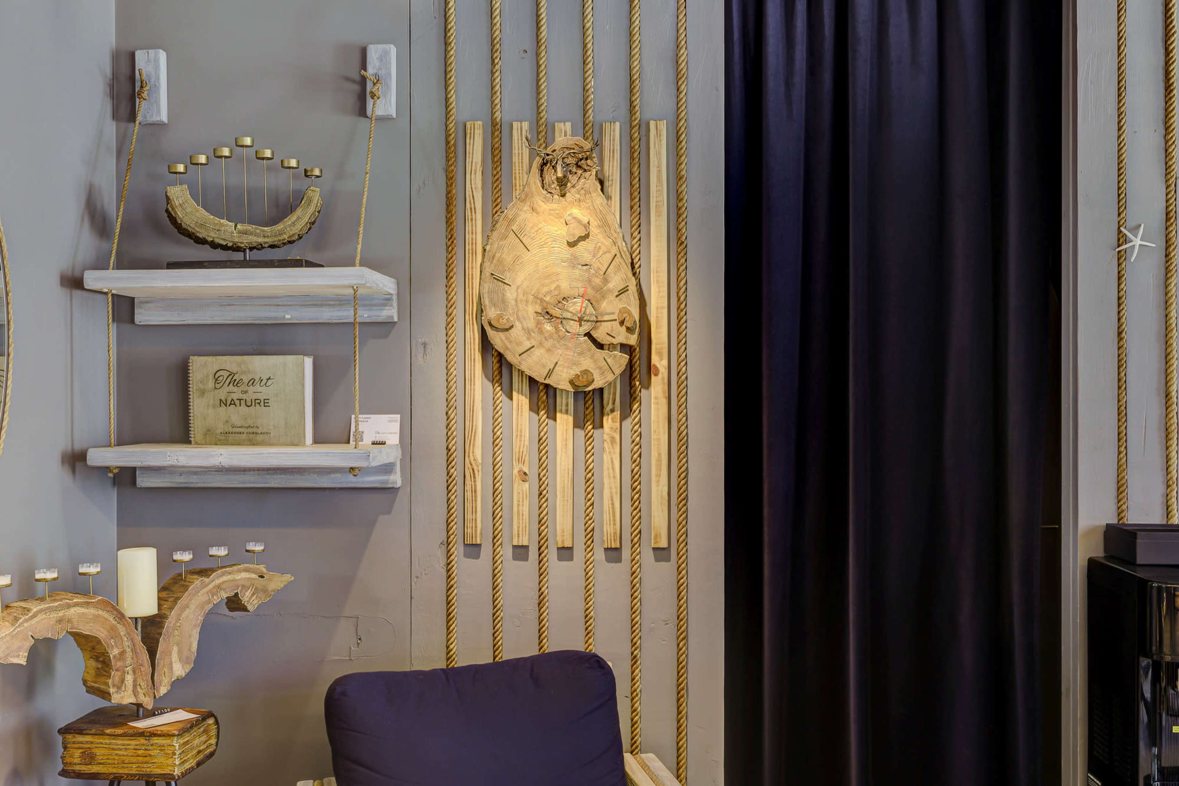 The image shows a stylish interior featuring a wall adorned with wooden shelves, decorative items, and a textured wood sculpture, alongside dark curtains and a cozy chair.