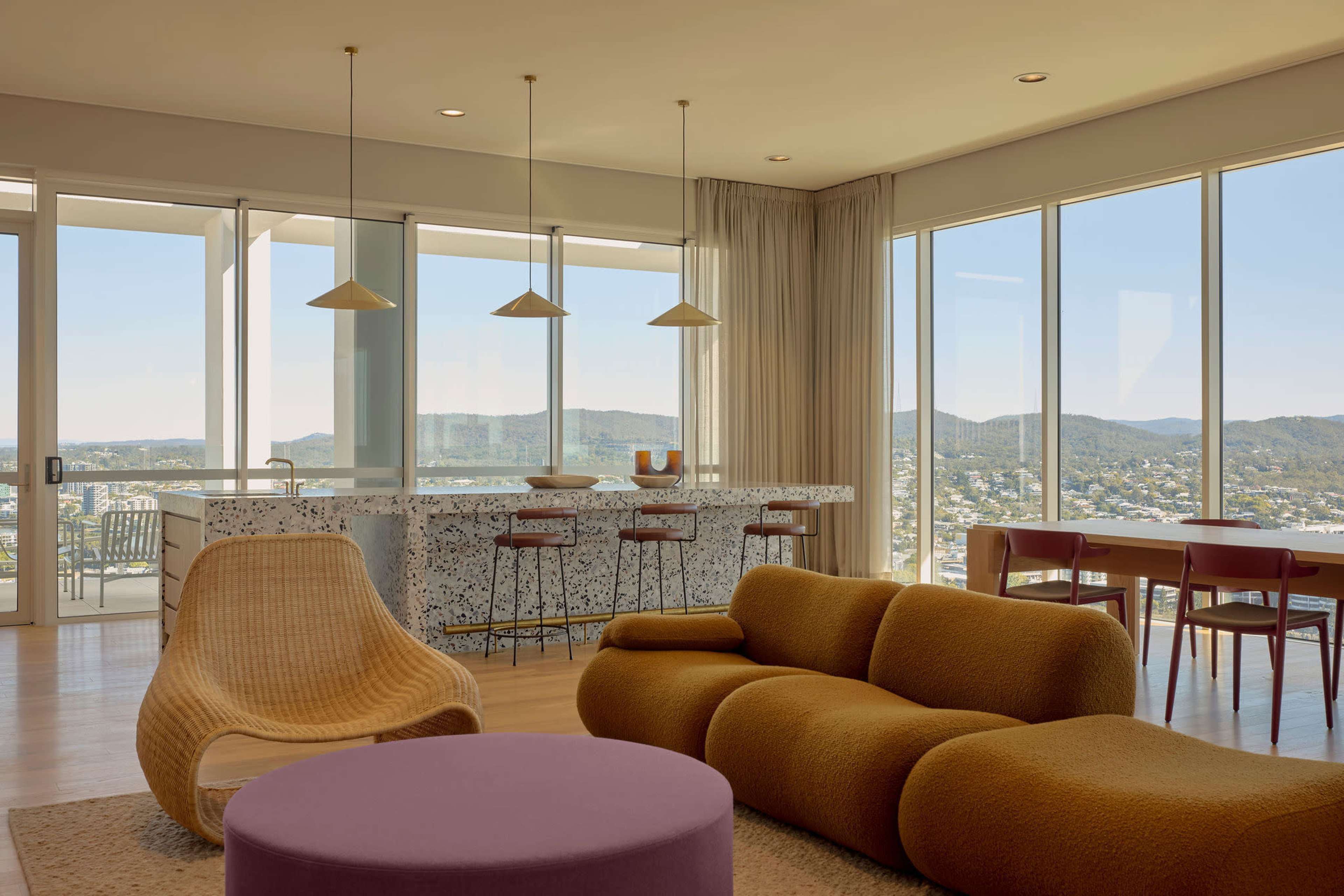 The image shows a modern, open-concept living space with large windows offering a panoramic view of distant hills.