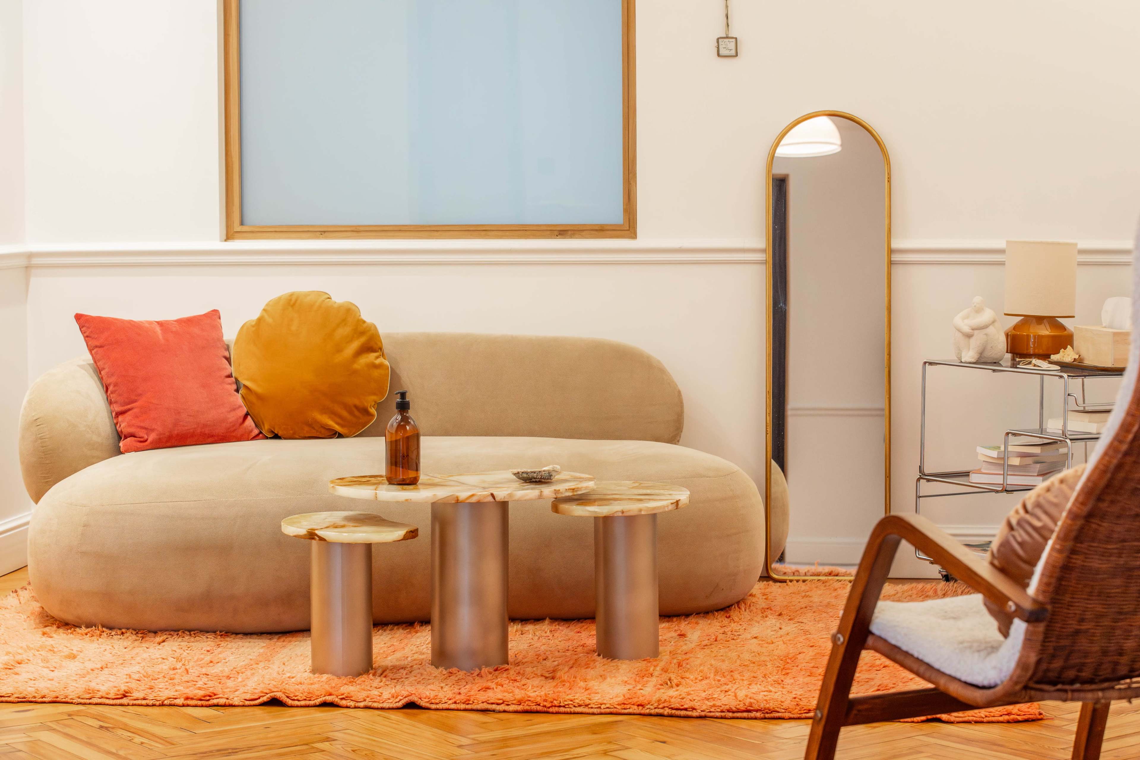 The image features a modern living room with a beige curved sofa, a marble coffee table with metallic legs, and a brown accent rug, complemented by a tall mirror and a decorative lamp.