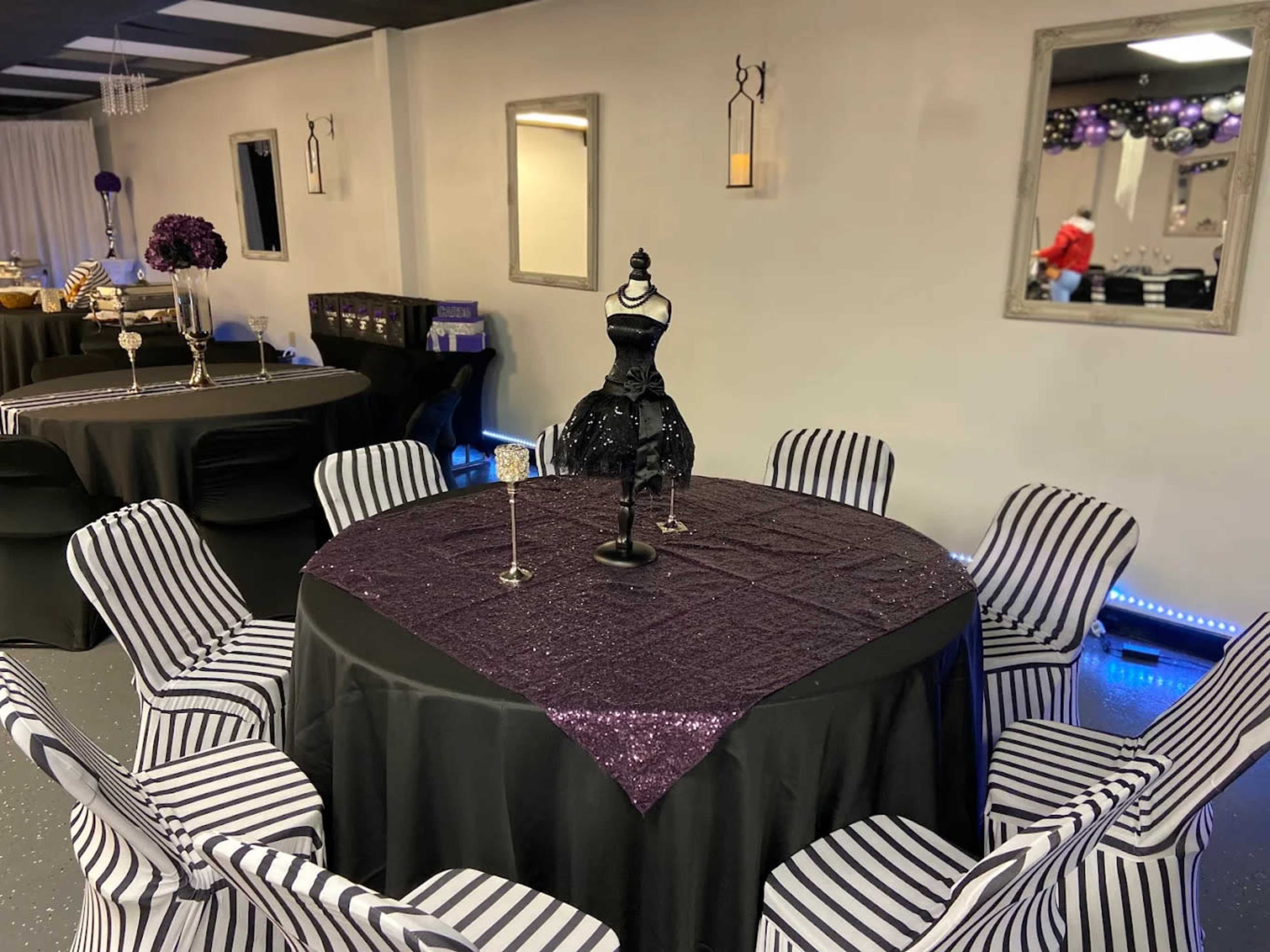 A banquet room is set up with a black tablecloth and striped chairs, featuring a decorative dress form centerpiece on a table.