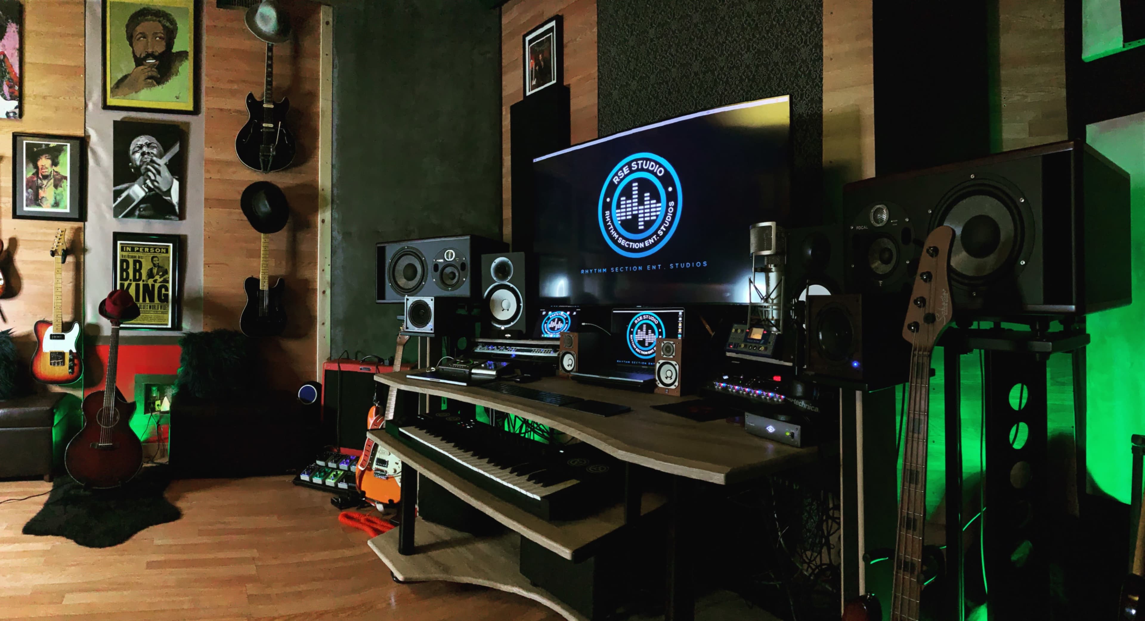 The image features a music studio equipped with various instruments, including guitars, a keyboard, and audio equipment, along with a large monitor displaying a logo.
