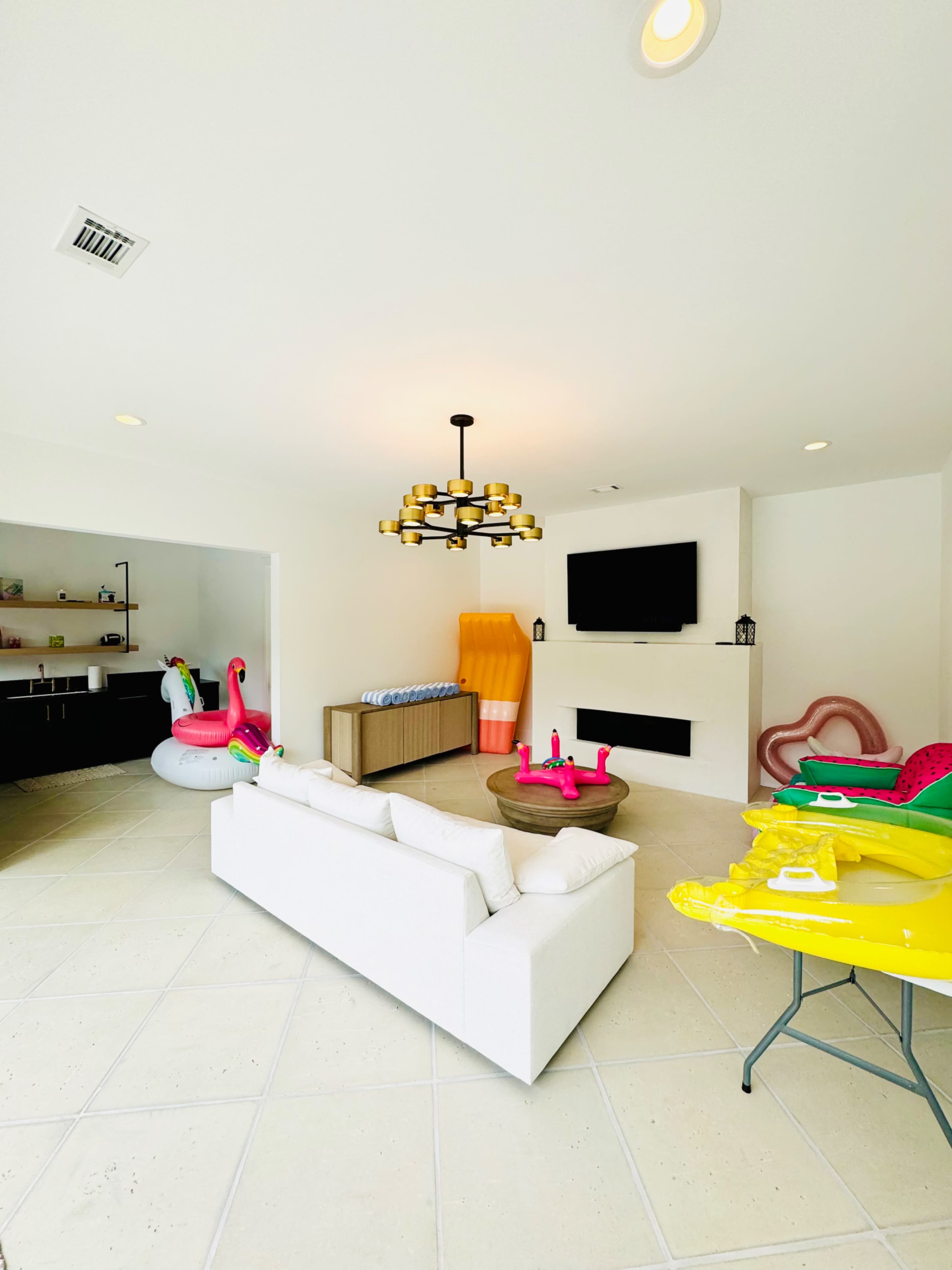 A bright living room features a white sofa, a wall-mounted TV, and colorful inflatable toys scattered around.