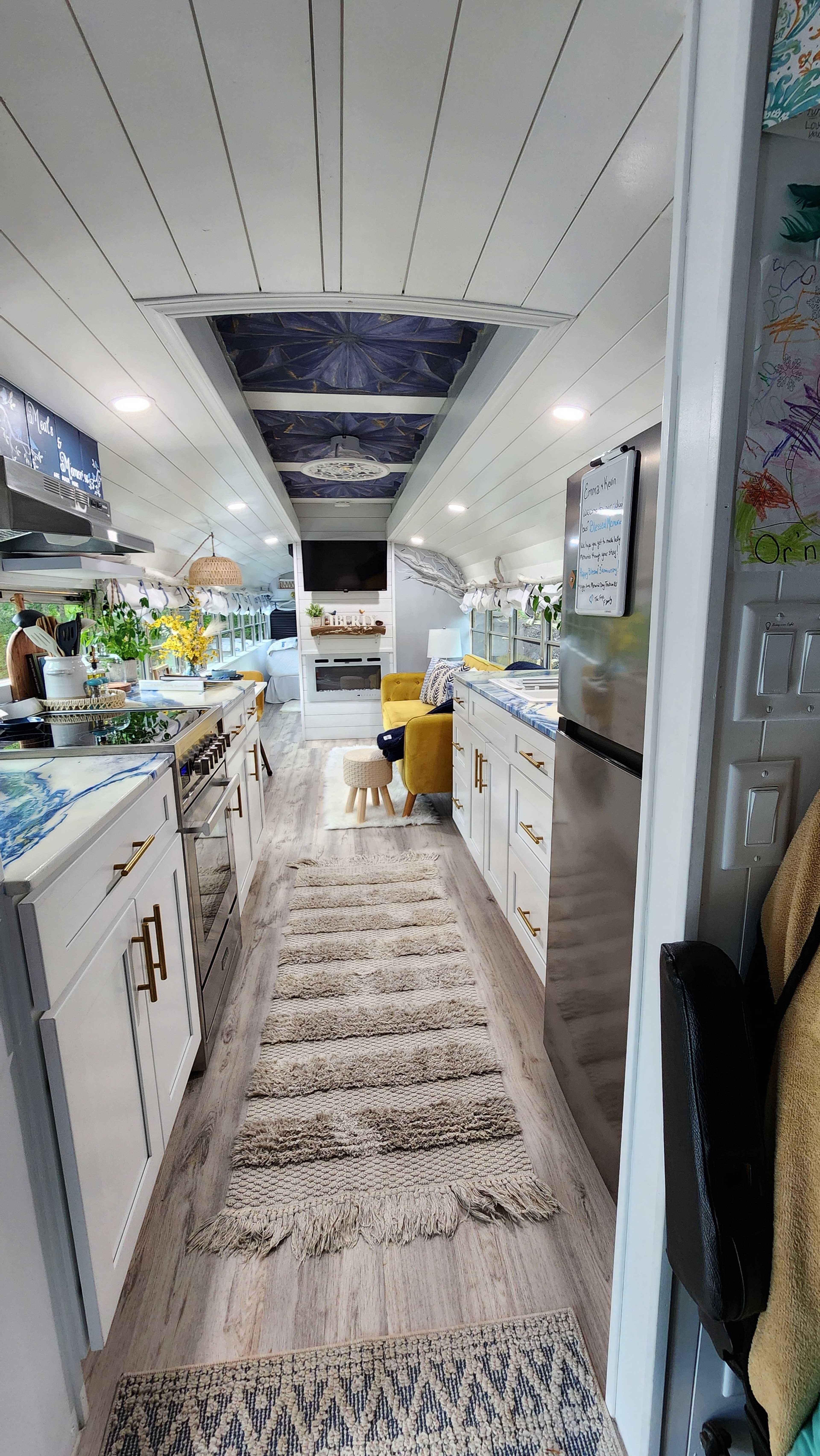The image shows a hallway-style kitchen with white cabinets, a patterned ceiling, and a rug running down the center.