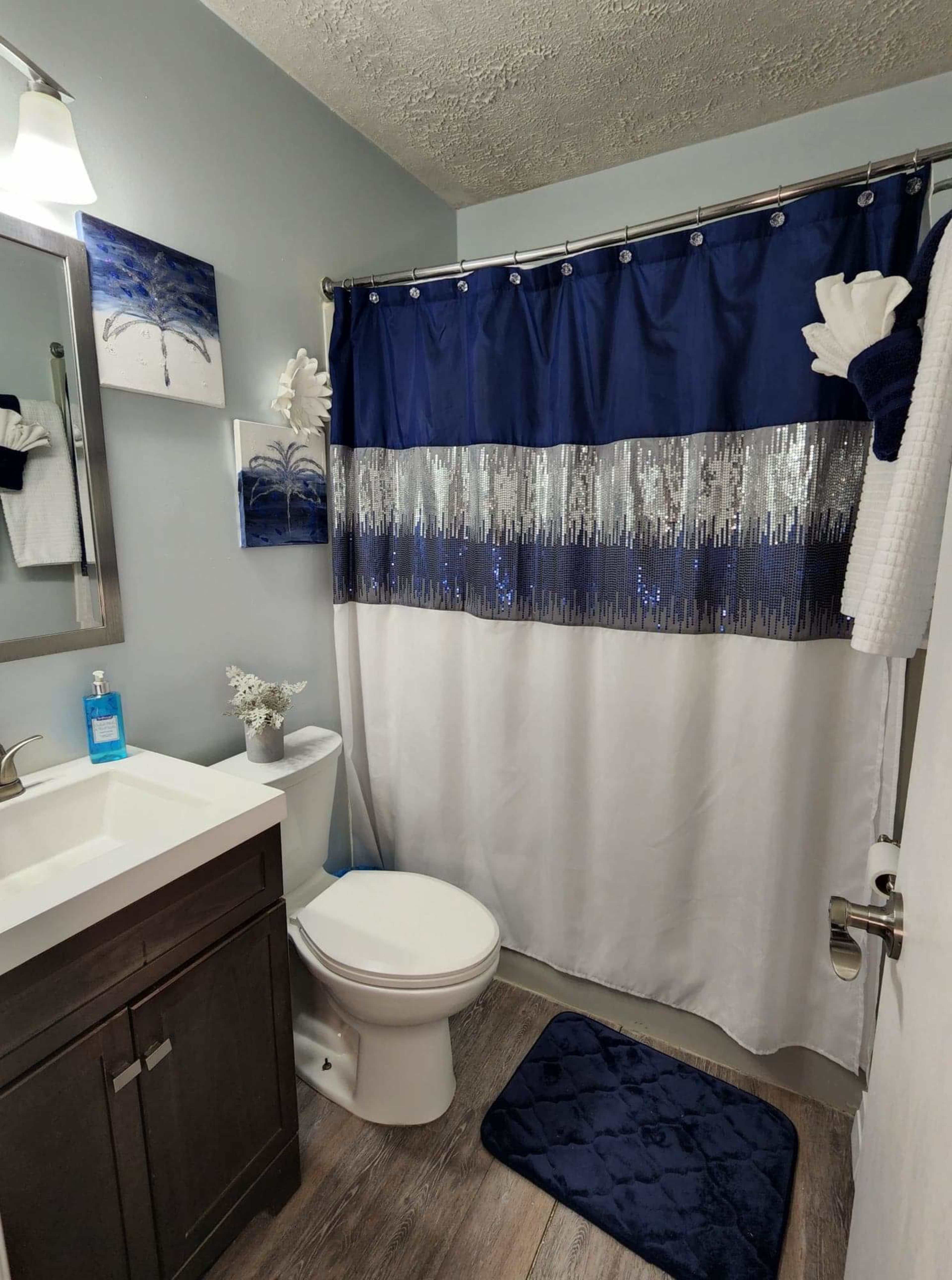 A modern bathroom with a blue and silver shower curtain, a white sink with a dark wood cabinet, and a toilet.