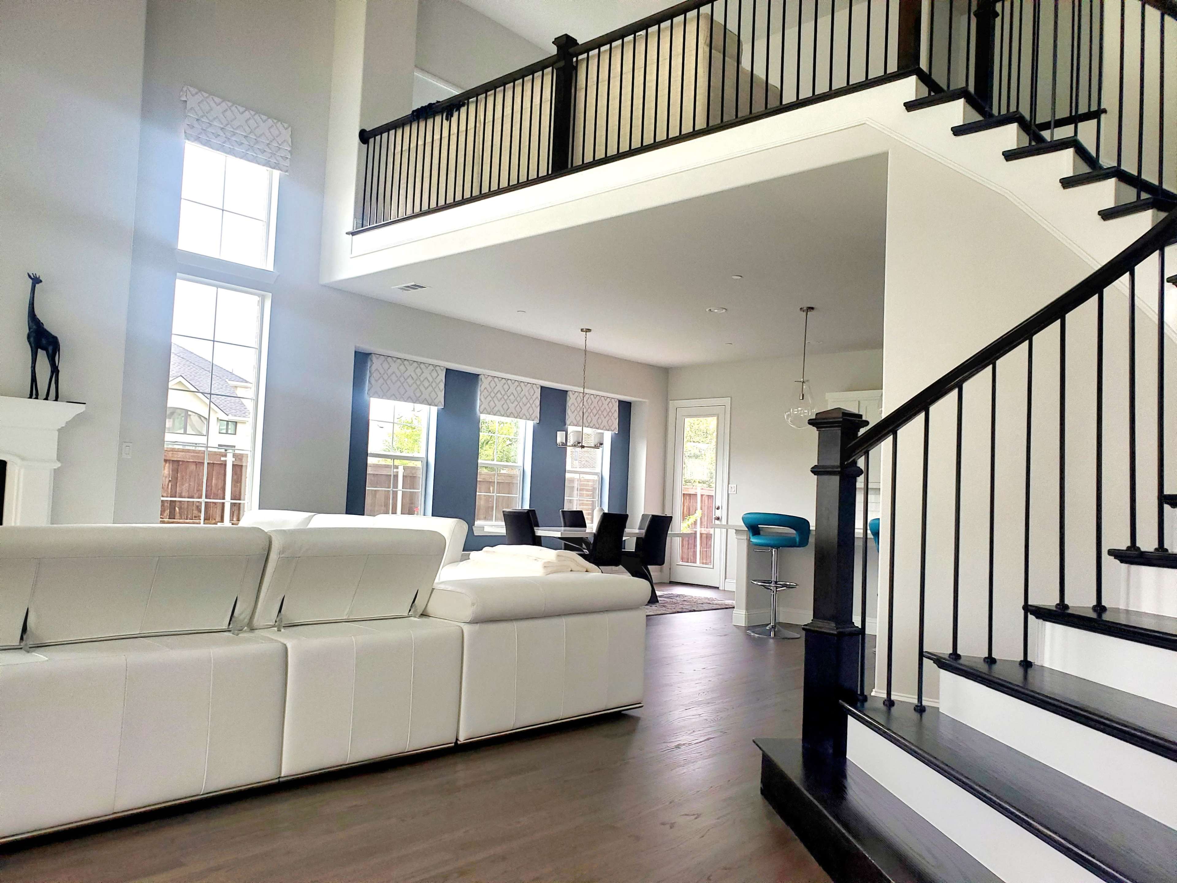 A modern living space with a white sectional sofa, a staircase leading to a balcony, and a dining area with a table and chairs.