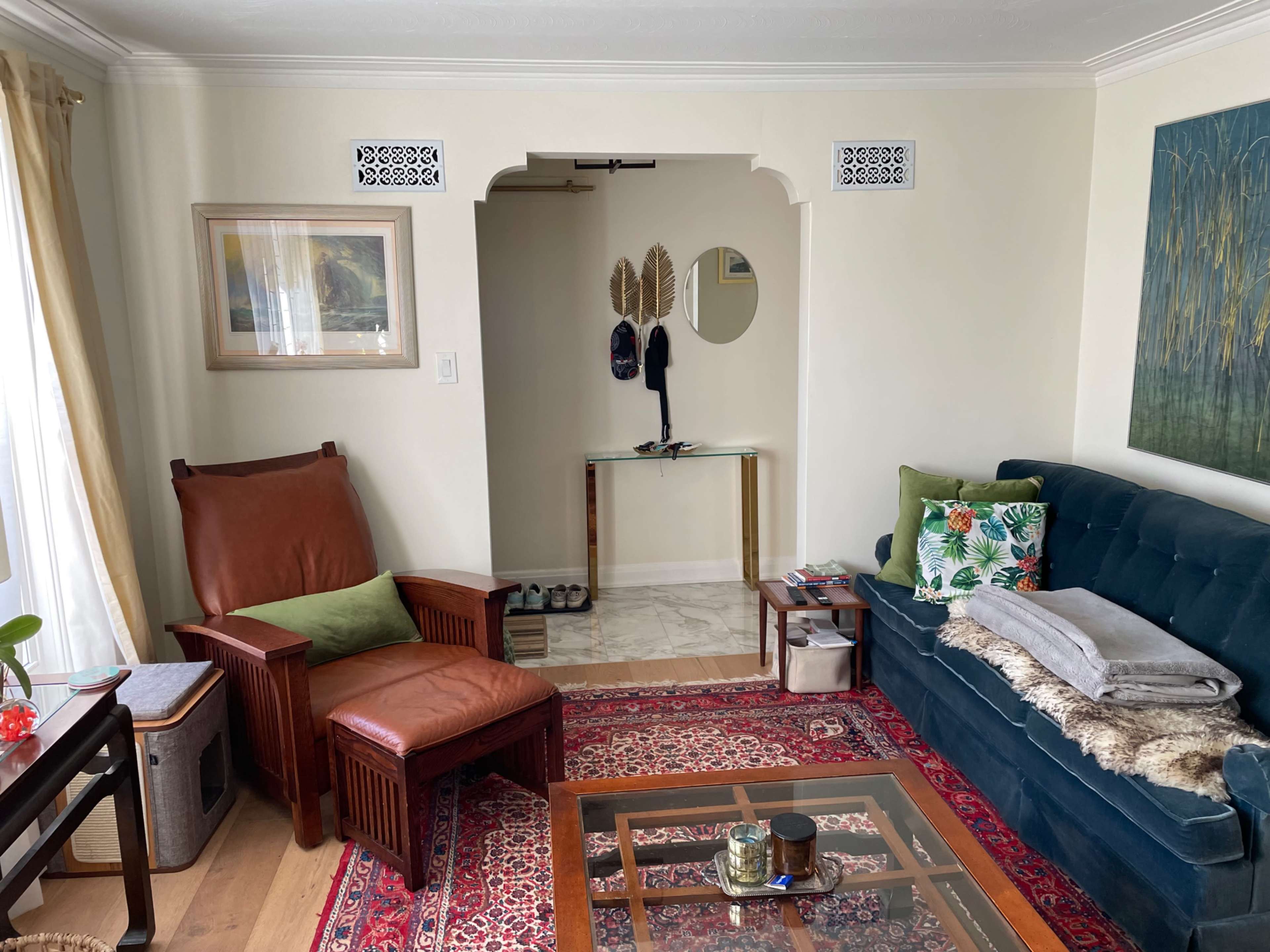 A living room with a green sofa, a brown leather chair, and an entryway leading to a small table and mirror.