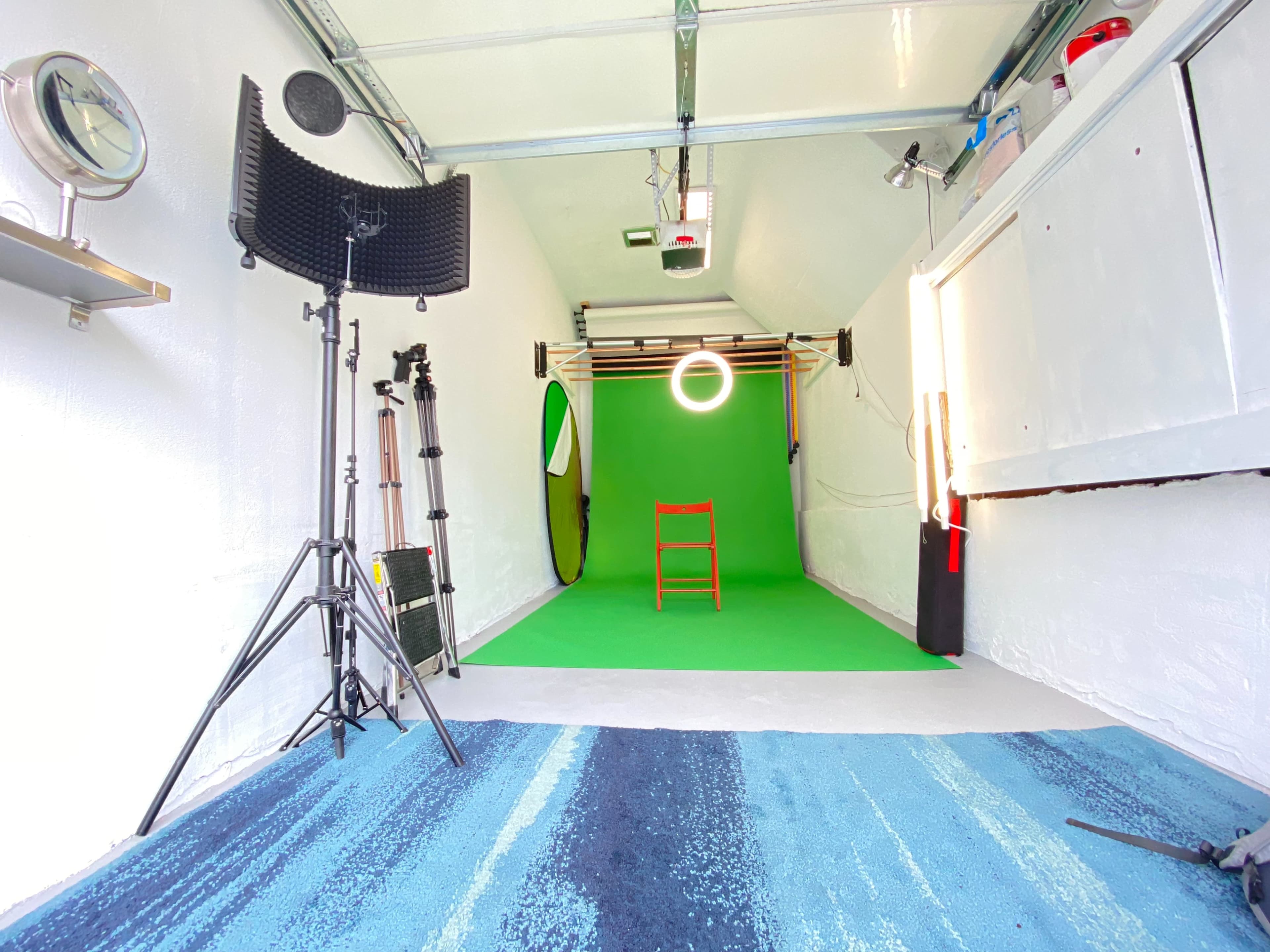 A studio space with a green backdrop, a red chair positioned in front, various lighting equipment, and a striped blue rug on the floor.