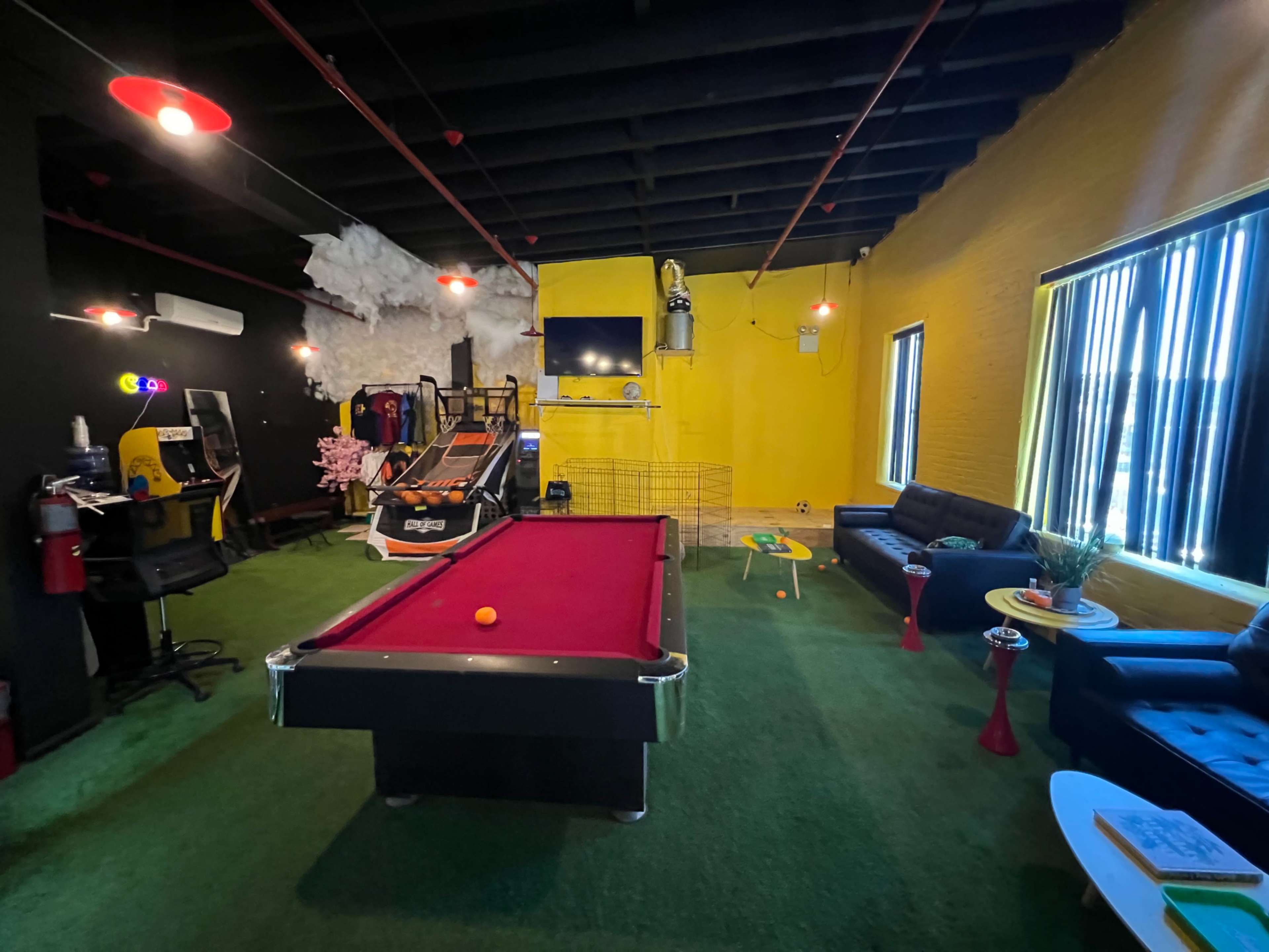 A recreational room featuring a pool table, arcade games, a turf floor, and a seating area with sofas and a coffee table.