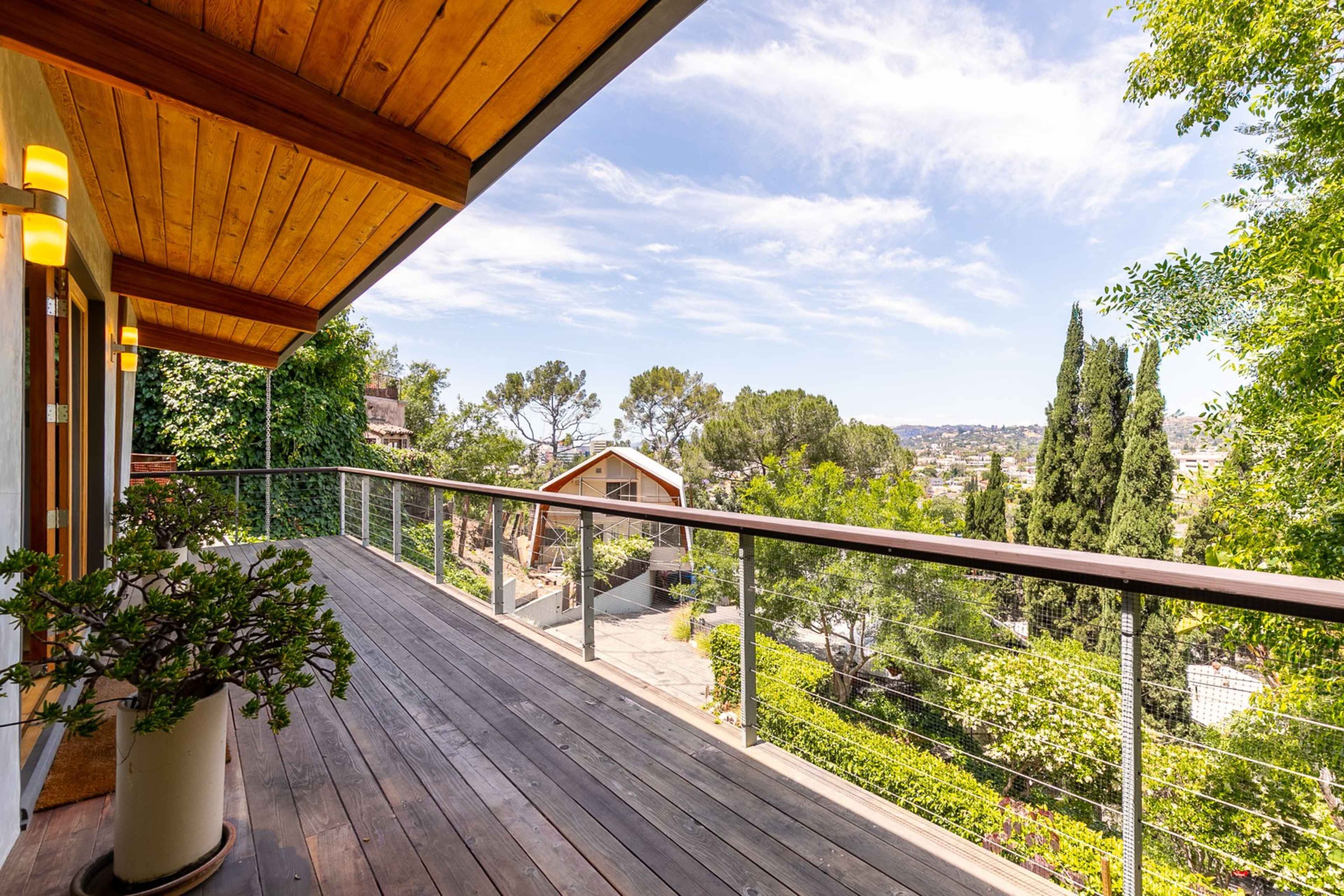 A spacious wooden deck with a railing overlooks a green landscape and distant hills under a blue sky.