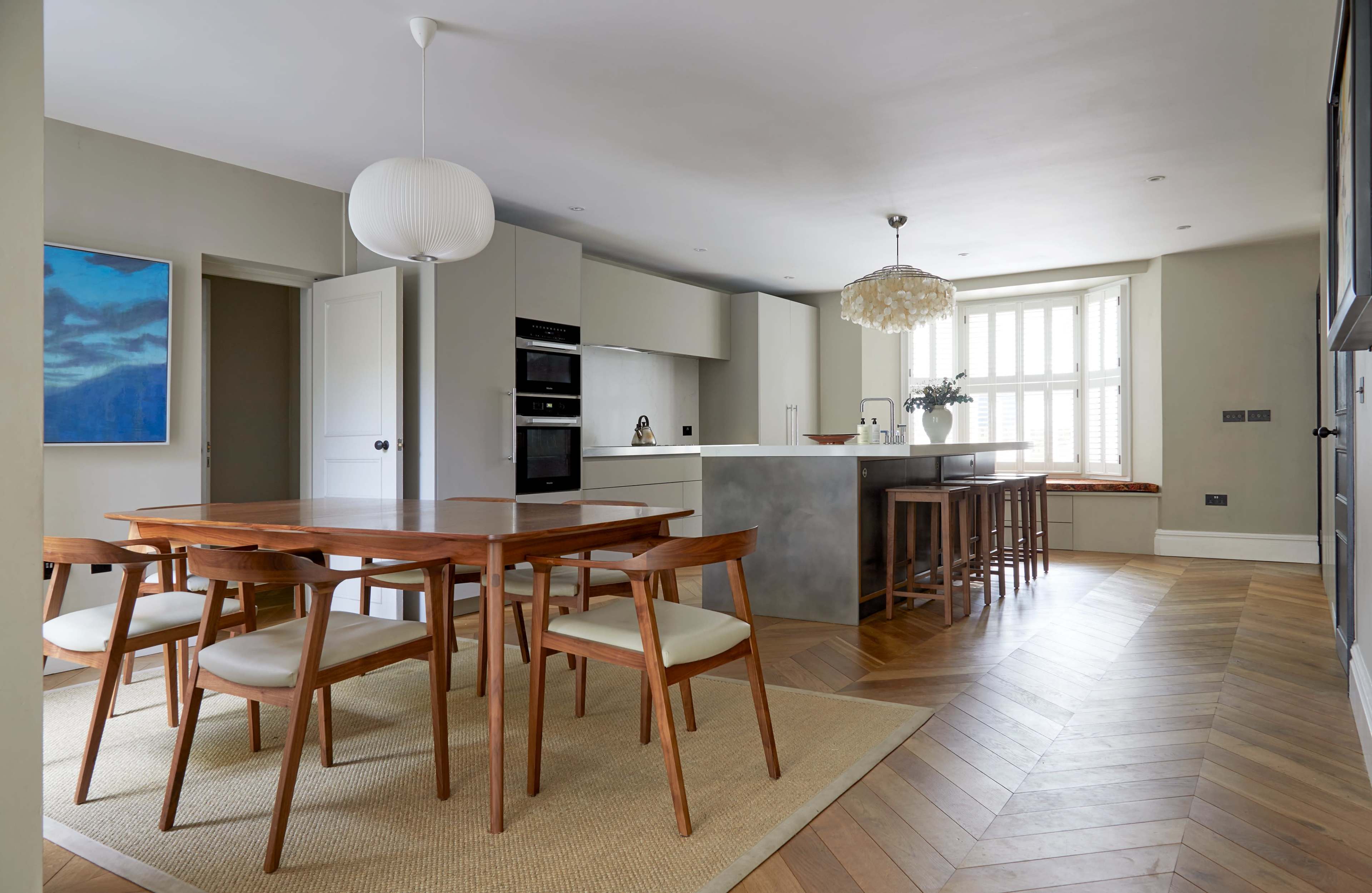 A modern kitchen dining area features a wooden table with chairs, a stylish kitchen island, and large windows allowing natural light.