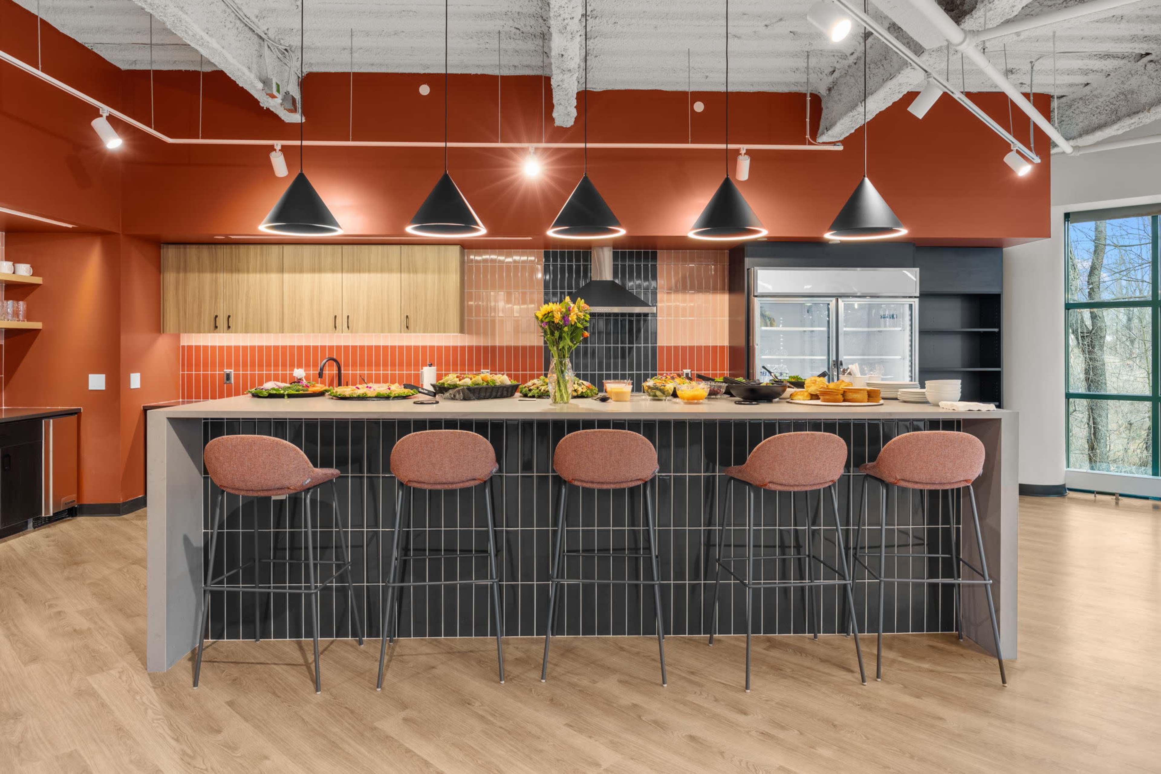A modern kitchen features a large island with bar stools, wooden cabinets, and pendant lighting against an orange and black backdrop.