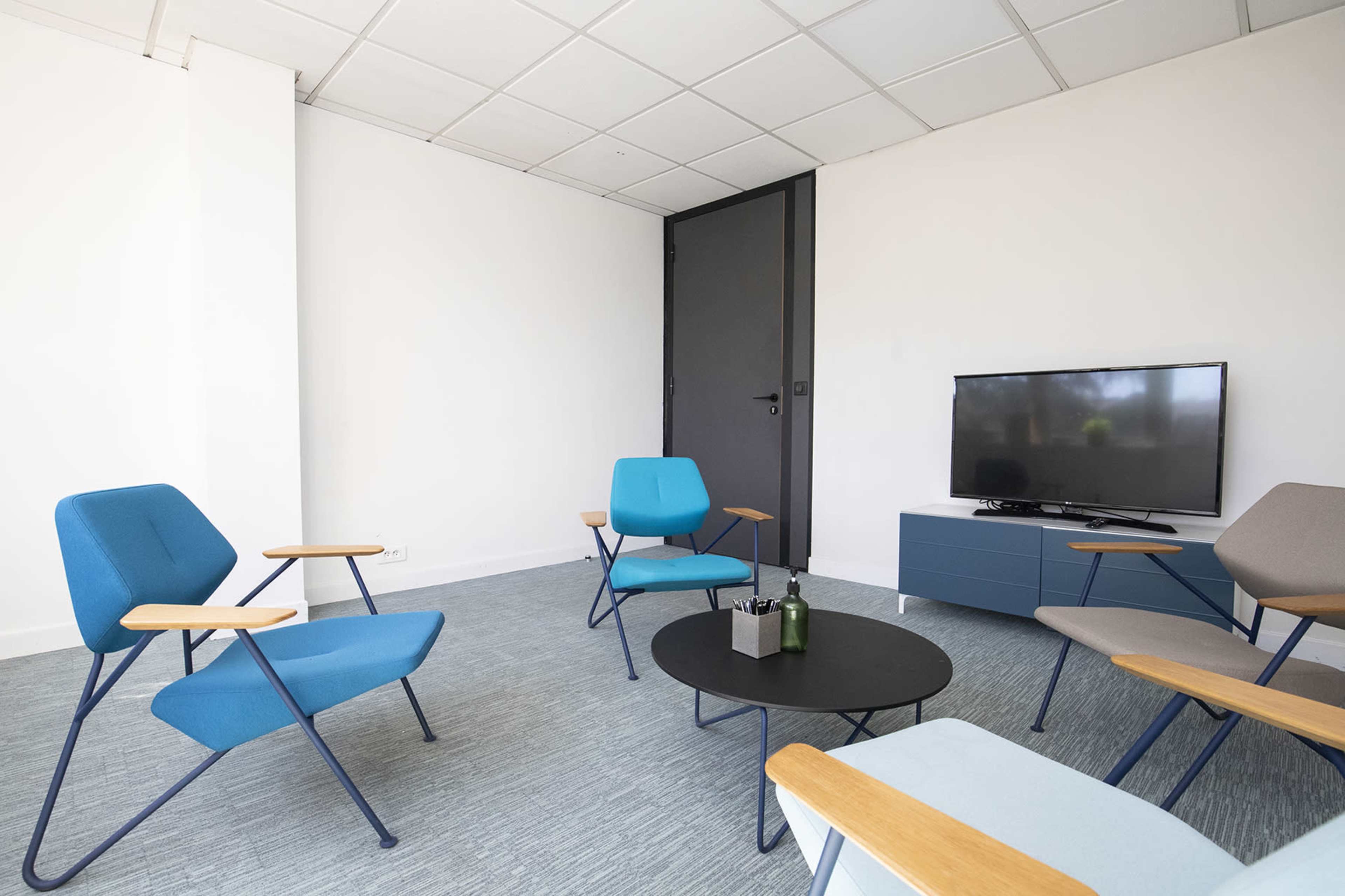 A modern seating area with four chairs, a small black coffee table, and a television against a white wall.