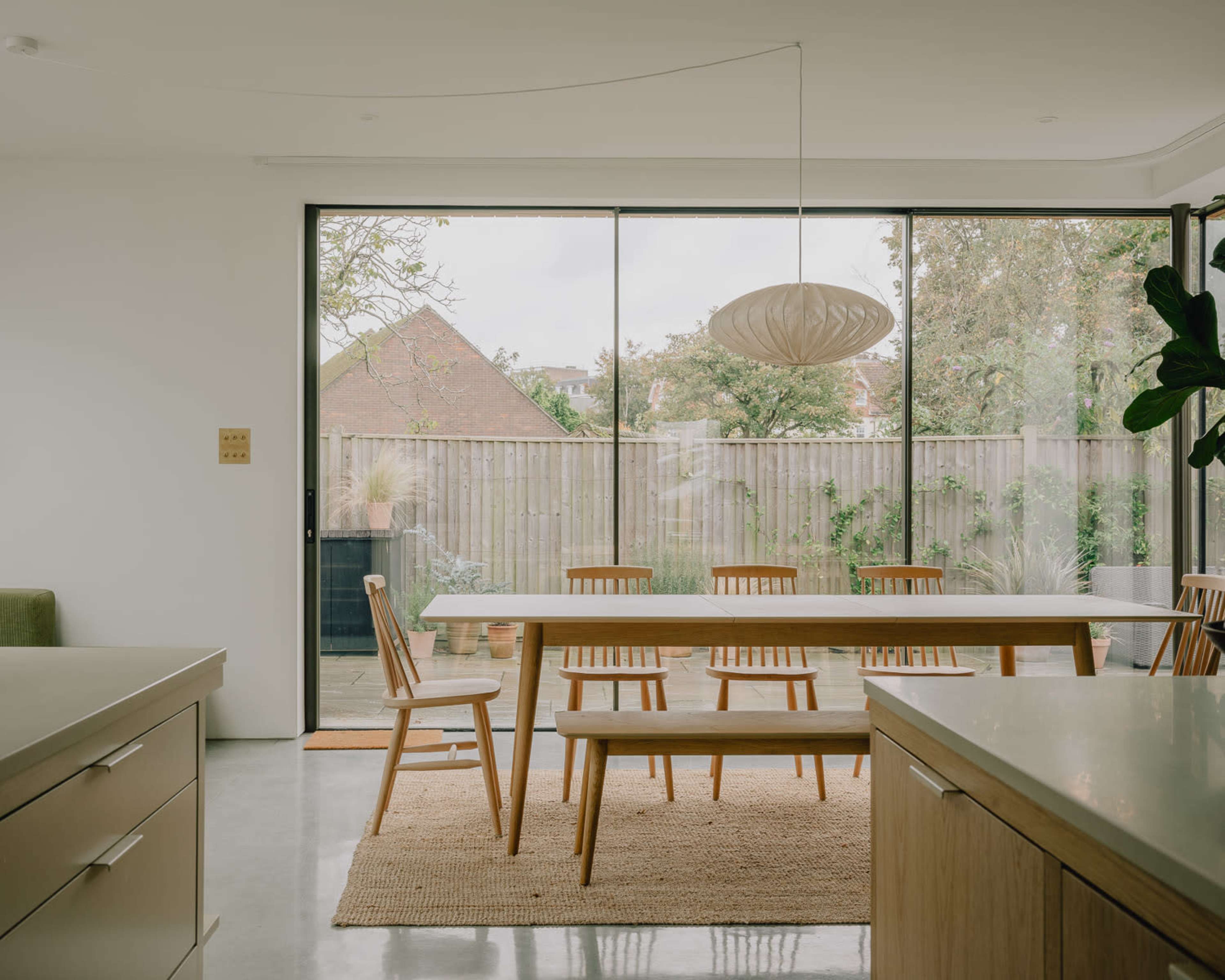 A modern kitchen features a wooden dining table and chairs, with large glass doors opening to a garden view.